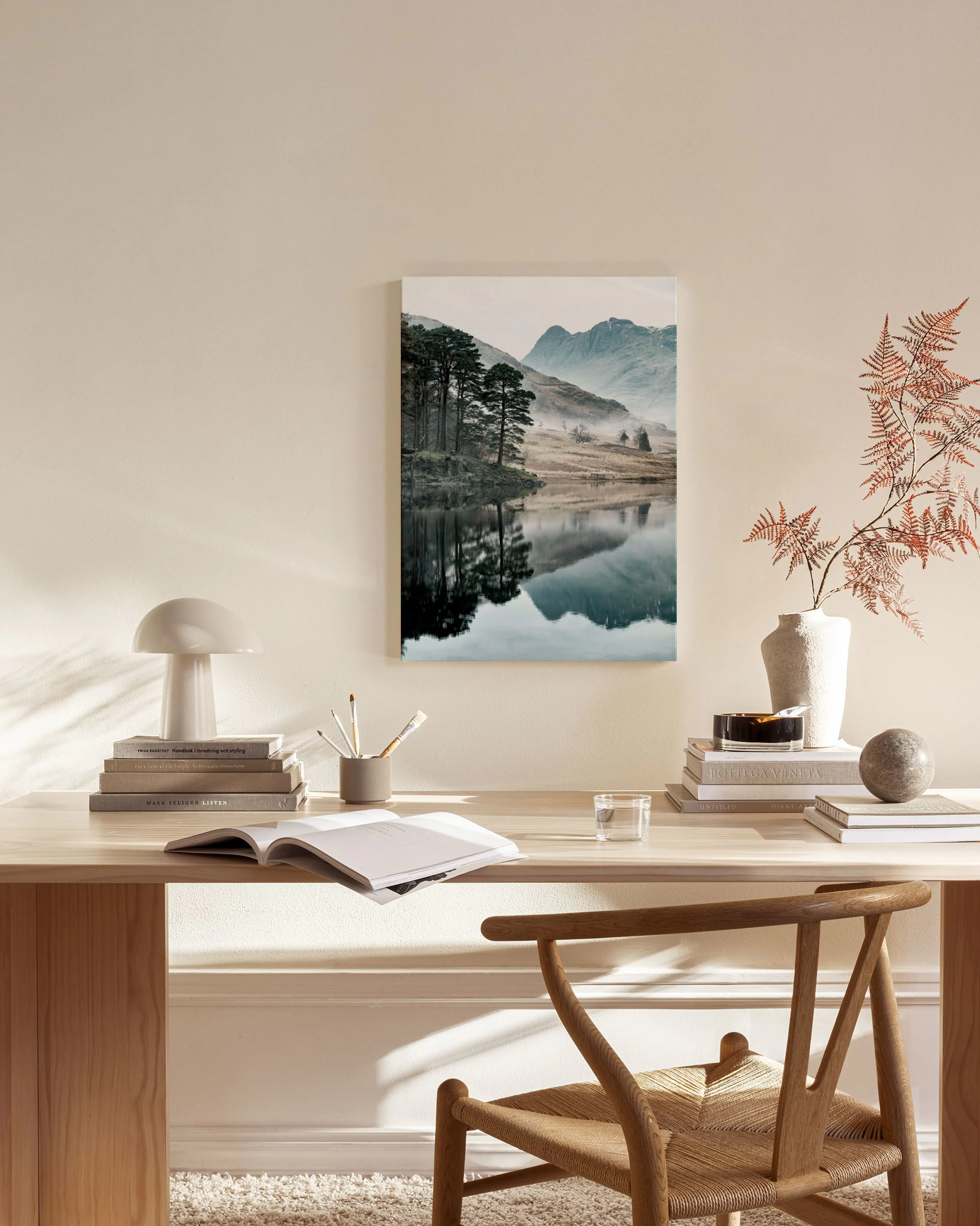 Leinwandbild einer nebligen Berglandschaft mit See und Nadelbäumen, über einem Sideboard in einem modernen Wohnzimmer hängend.