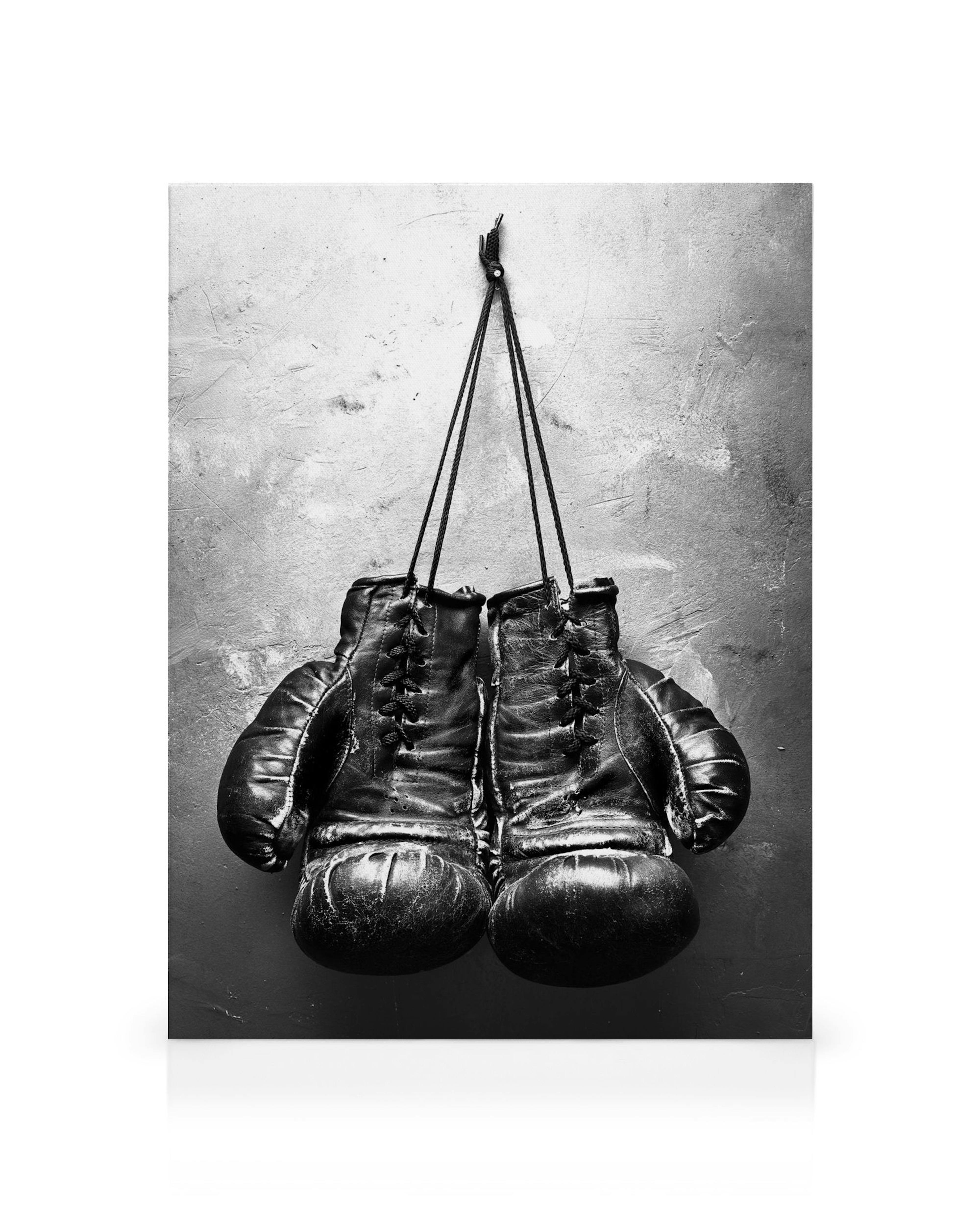 Guantoni da boxe neri usurati appesi a un chiodo su parete grigia, stampa monocromatica
