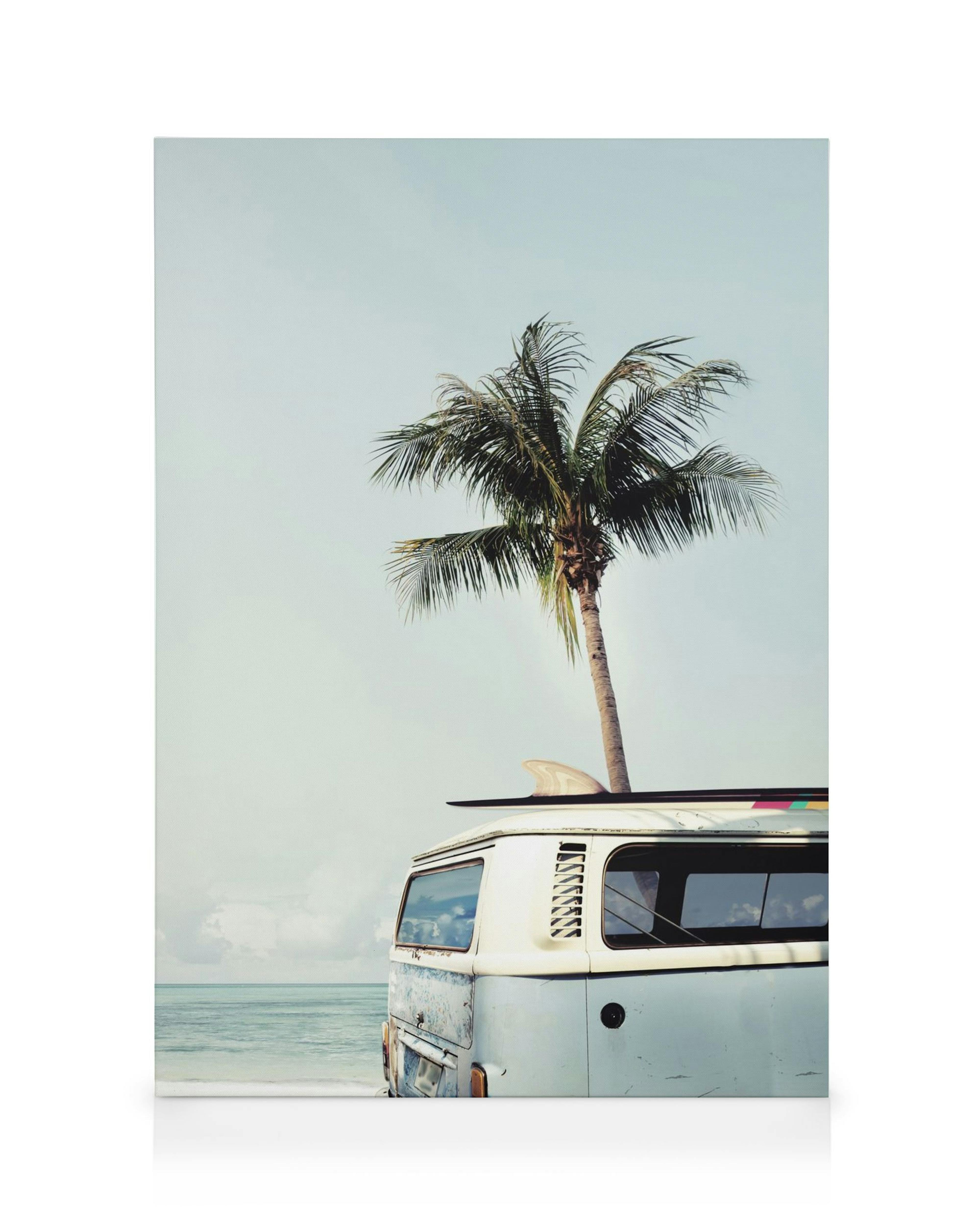 Vintage surf van with surfboard on roof, parked on a beach with a palm tree, ocean in background, retro summer scene.
