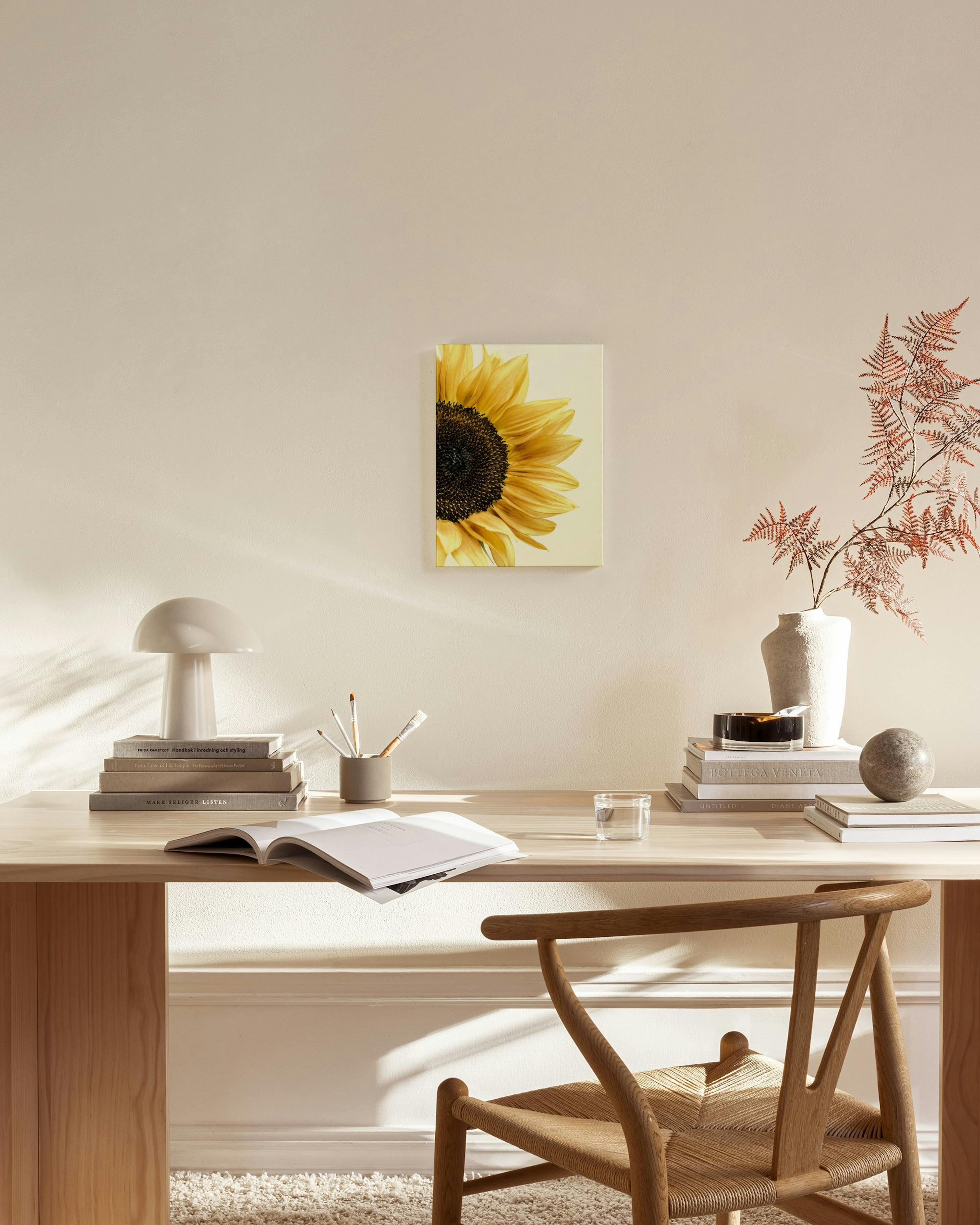 Stampa su tela di un girasole giallo brillante, appesa in un soggiorno moderno sopra una credenza in legno naturale.