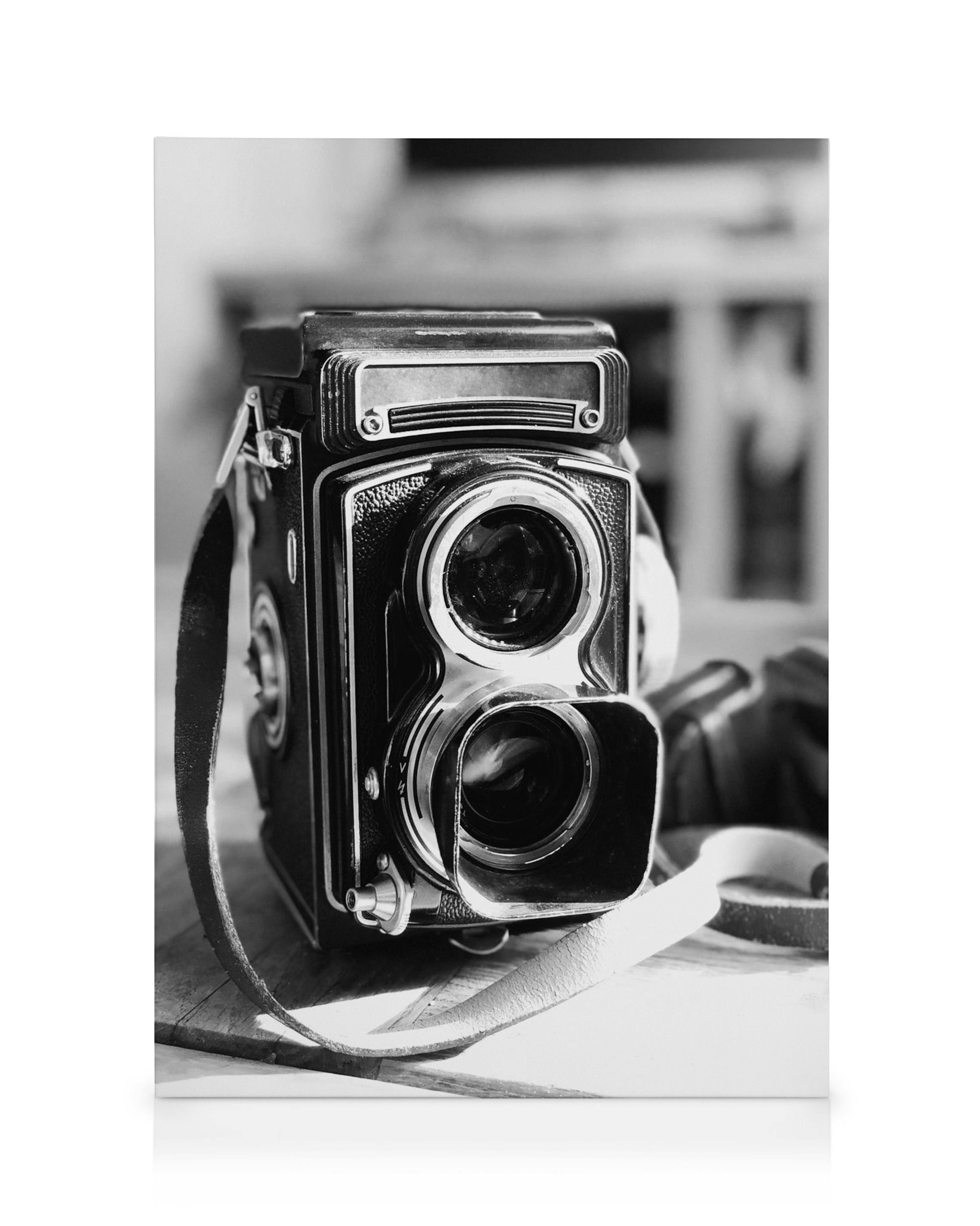Leinwandbild: Schwarz-weiße Vintage-Kamera mit Ledertragegurt, fokussiert auf die Vorderseite der Kamera.