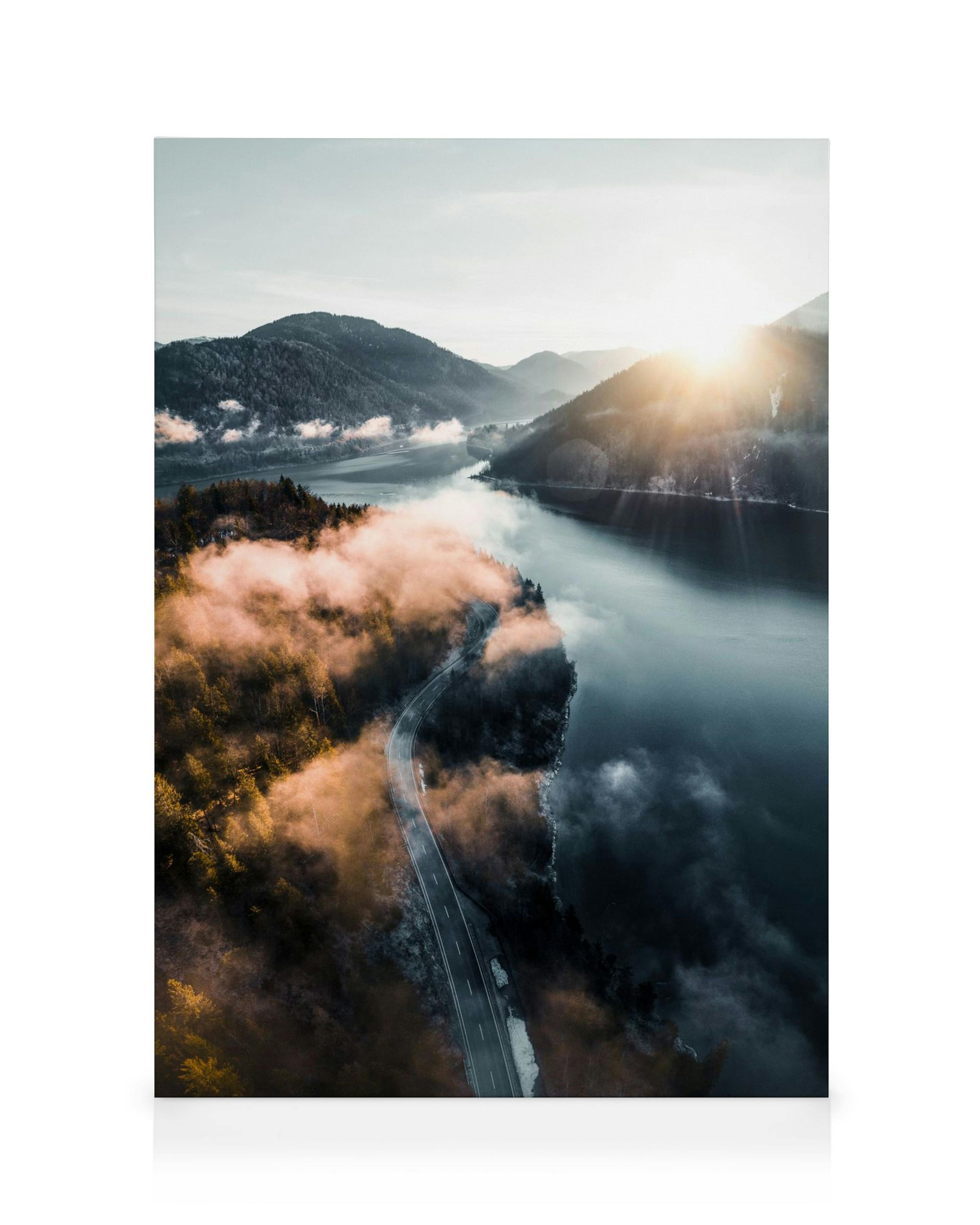 Weg langs rivier in herfstbos met bergen en mist, zonlicht gloeit over het landschap in blauw, groen, bruin.