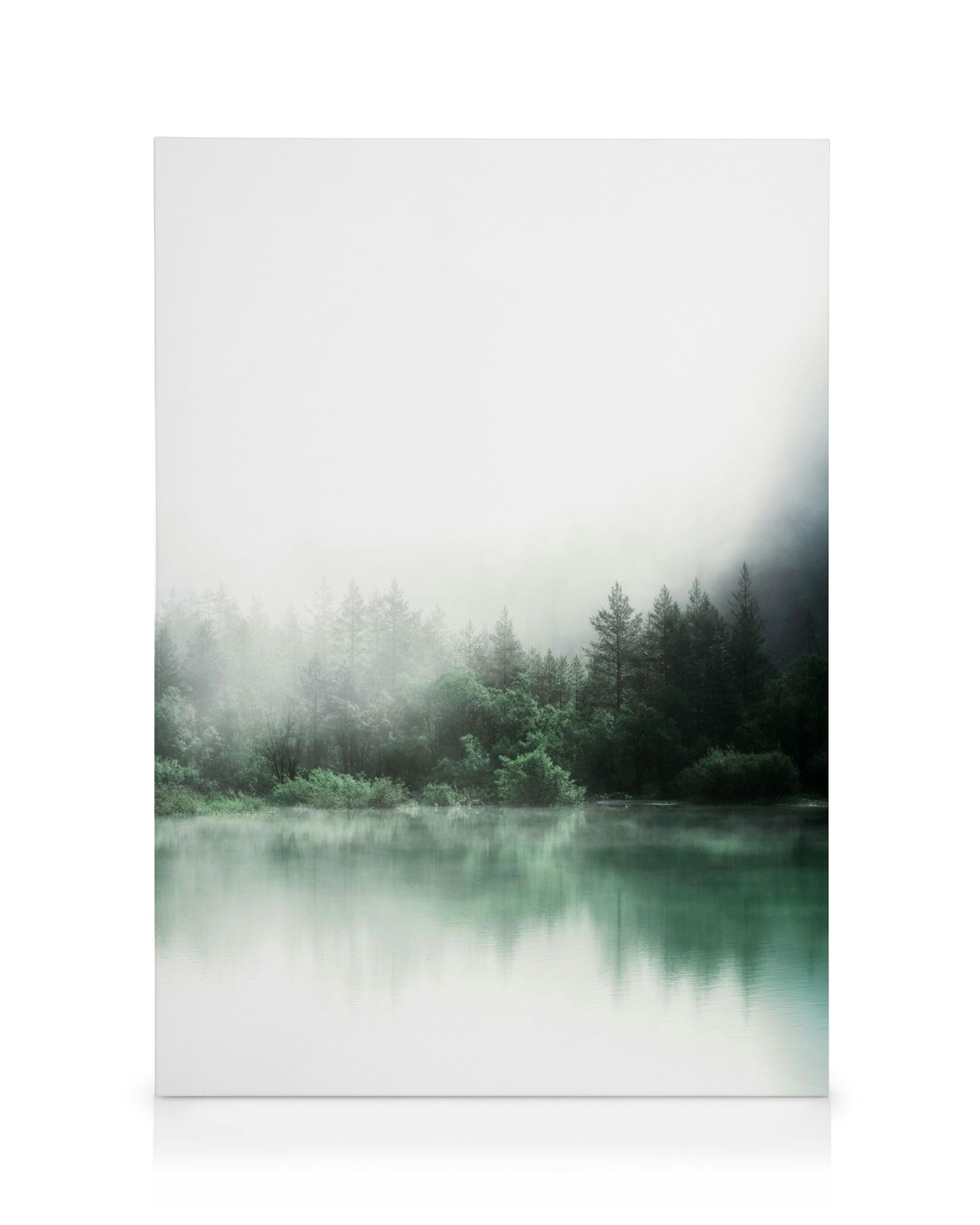Misty forest landscape canvas with green trees reflected on a calm, turquoise lake under a hazy sky.