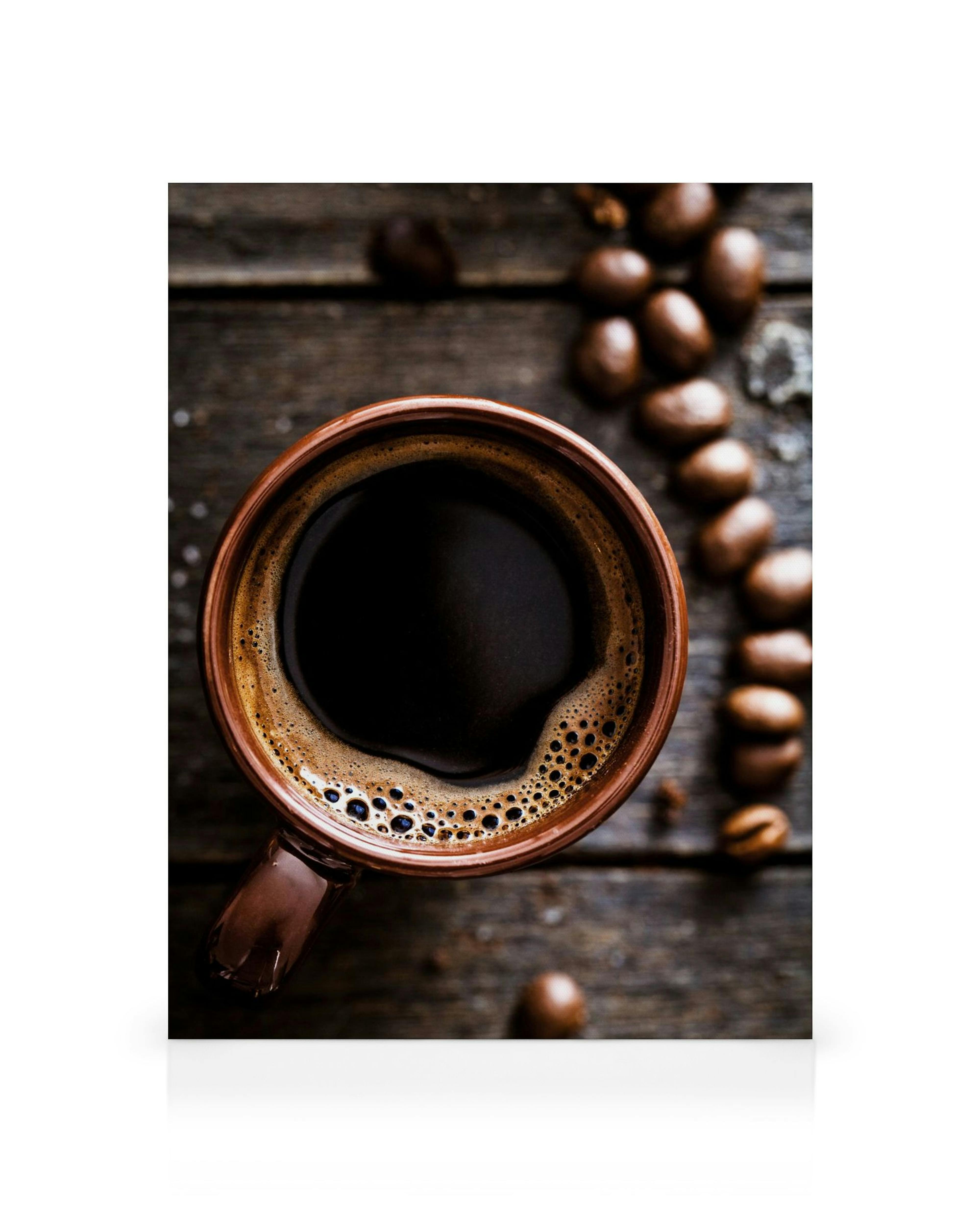 Canvas print of a coffee cup with dark coffee and foam on a rustic wooden table with scattered coffee beans.