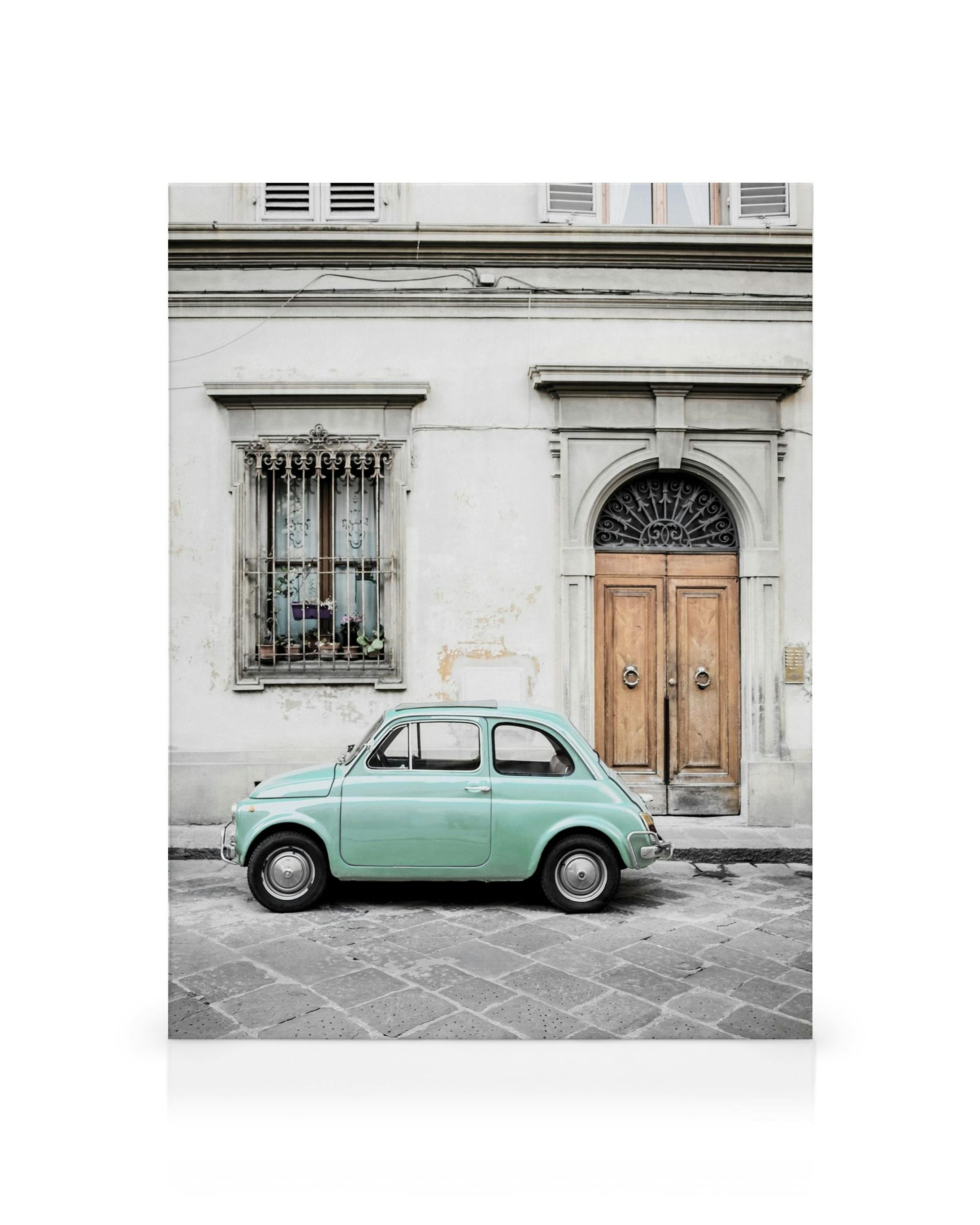Mintgrøn Fiat 500 parkeret på brosten foran en italiensk bygning med trædøre.