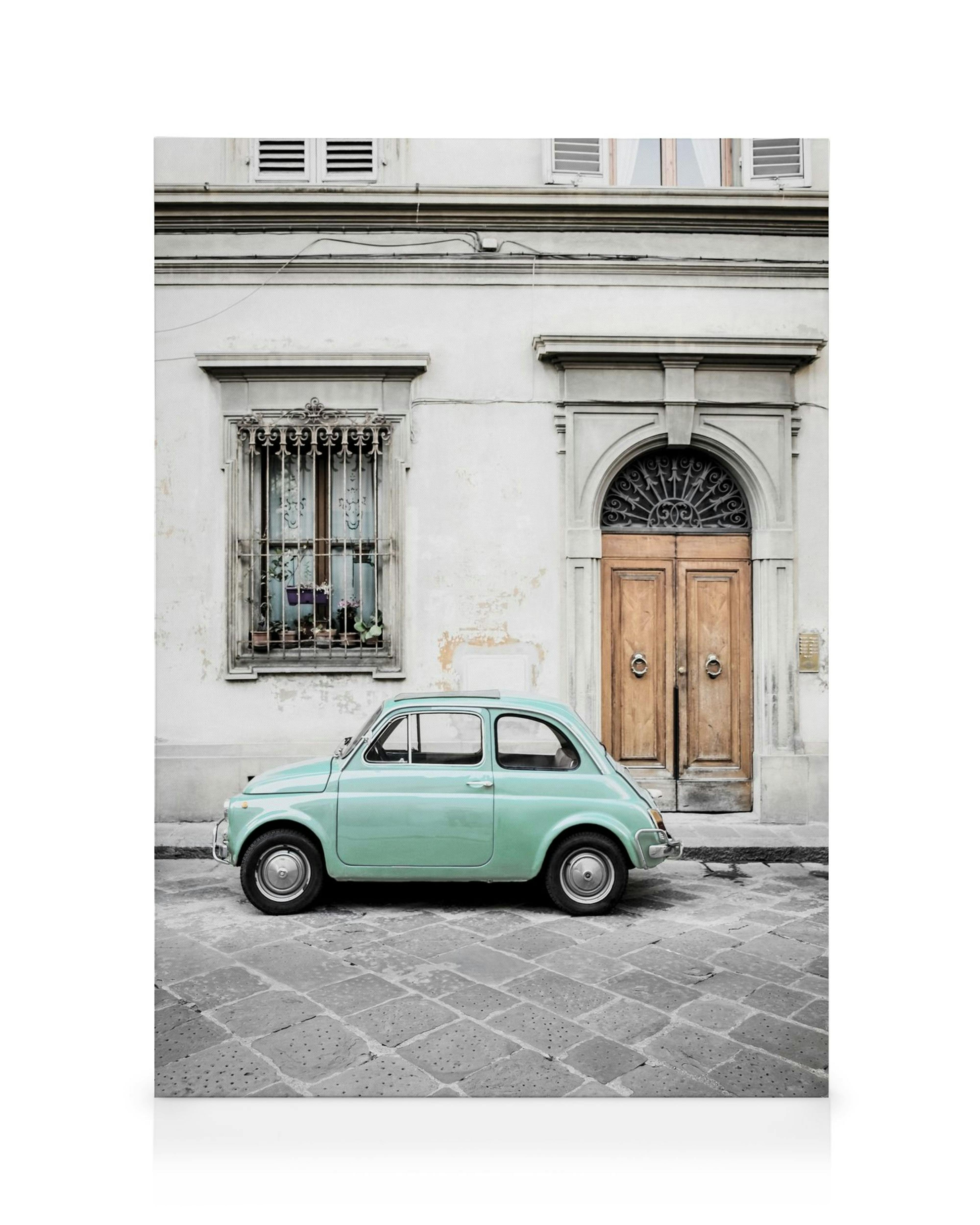 Vintage green car parked on a cobblestone street in Italy, with a charming old building background, perfect wall art.