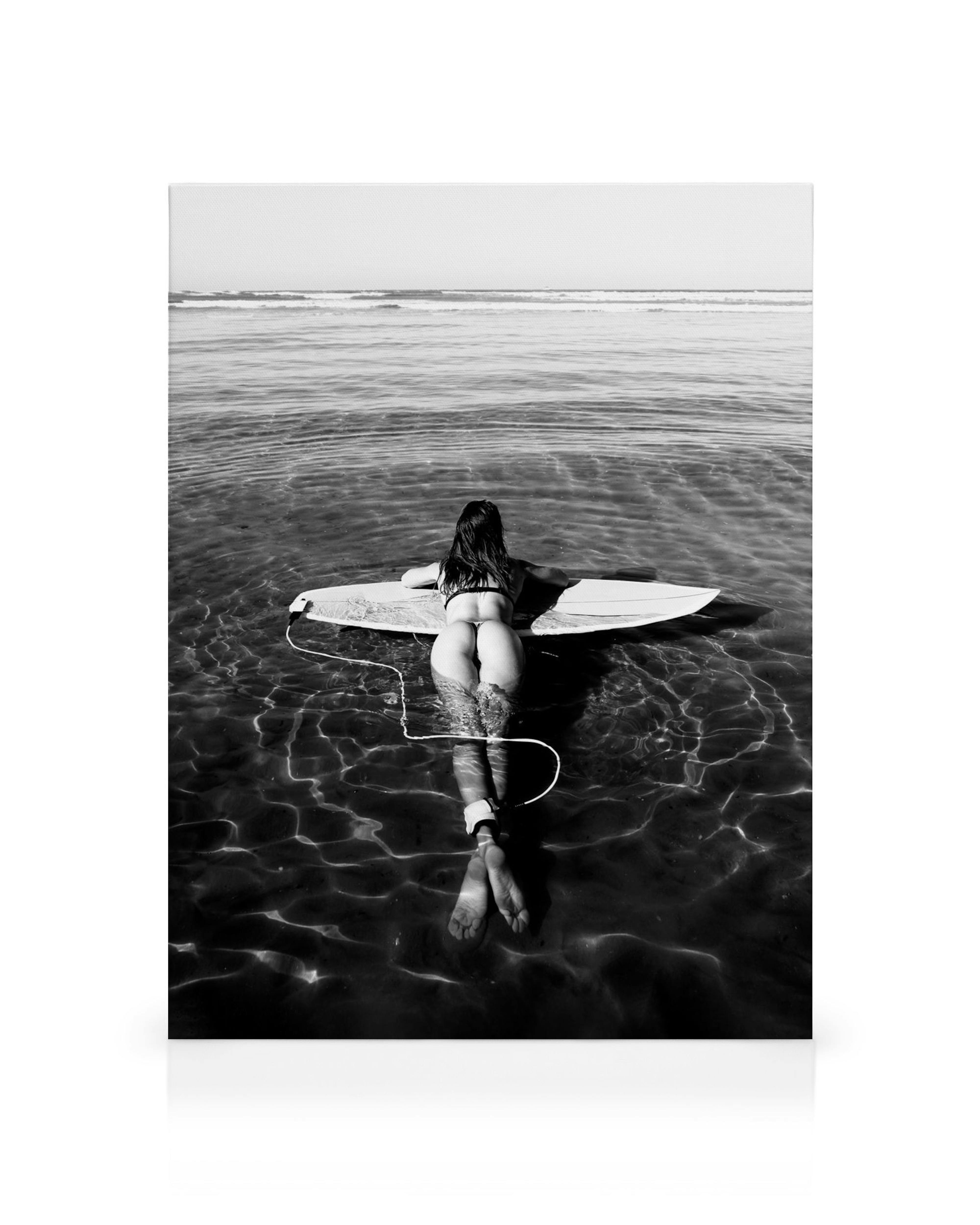 Black and white canvas print of a surfer floating on a surfboard in the ocean, with water ripples and waves.