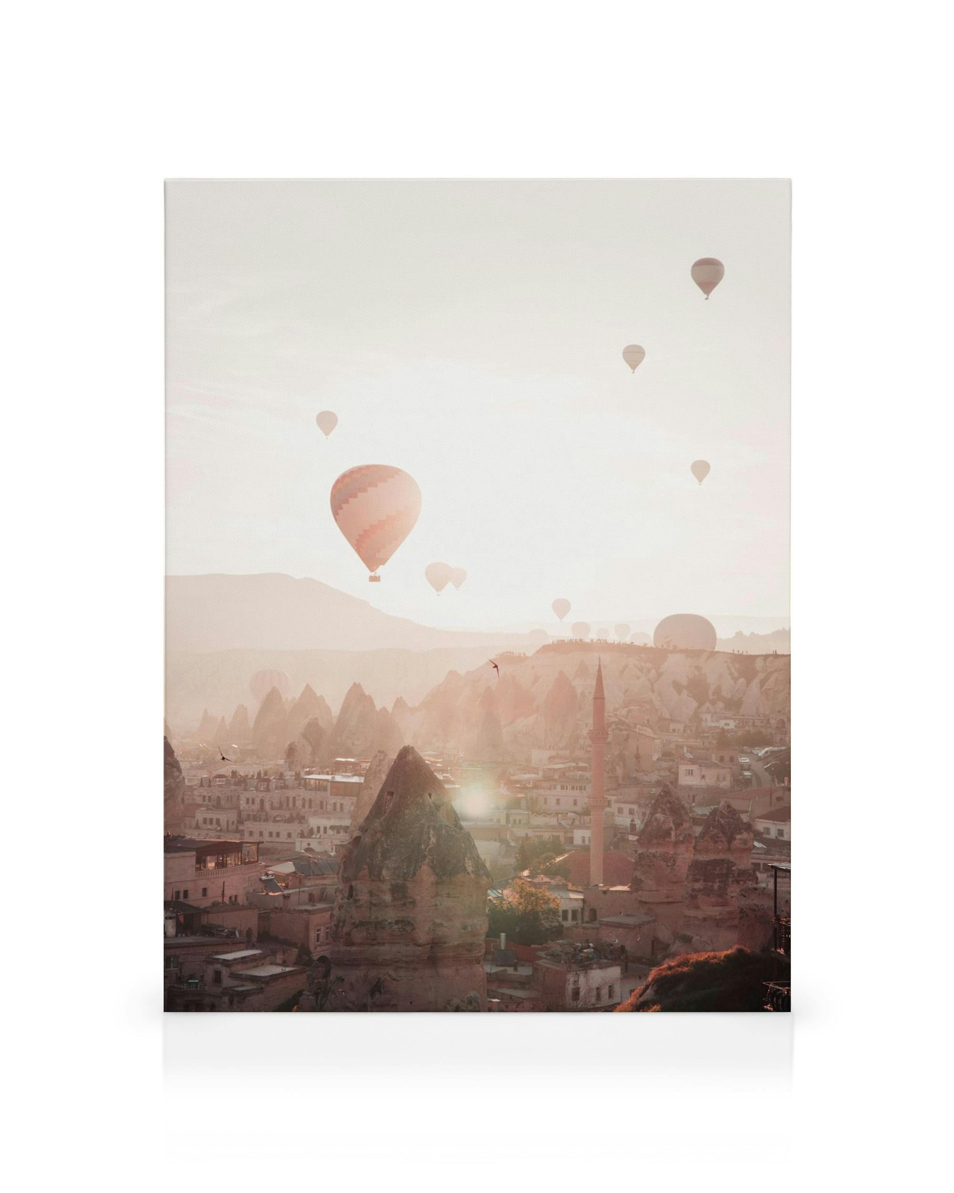 Heissluftballons schweben über die Felsformationen und Häuser von Kappadokien bei Sonnenaufgang, goldene Lichtstimmung.