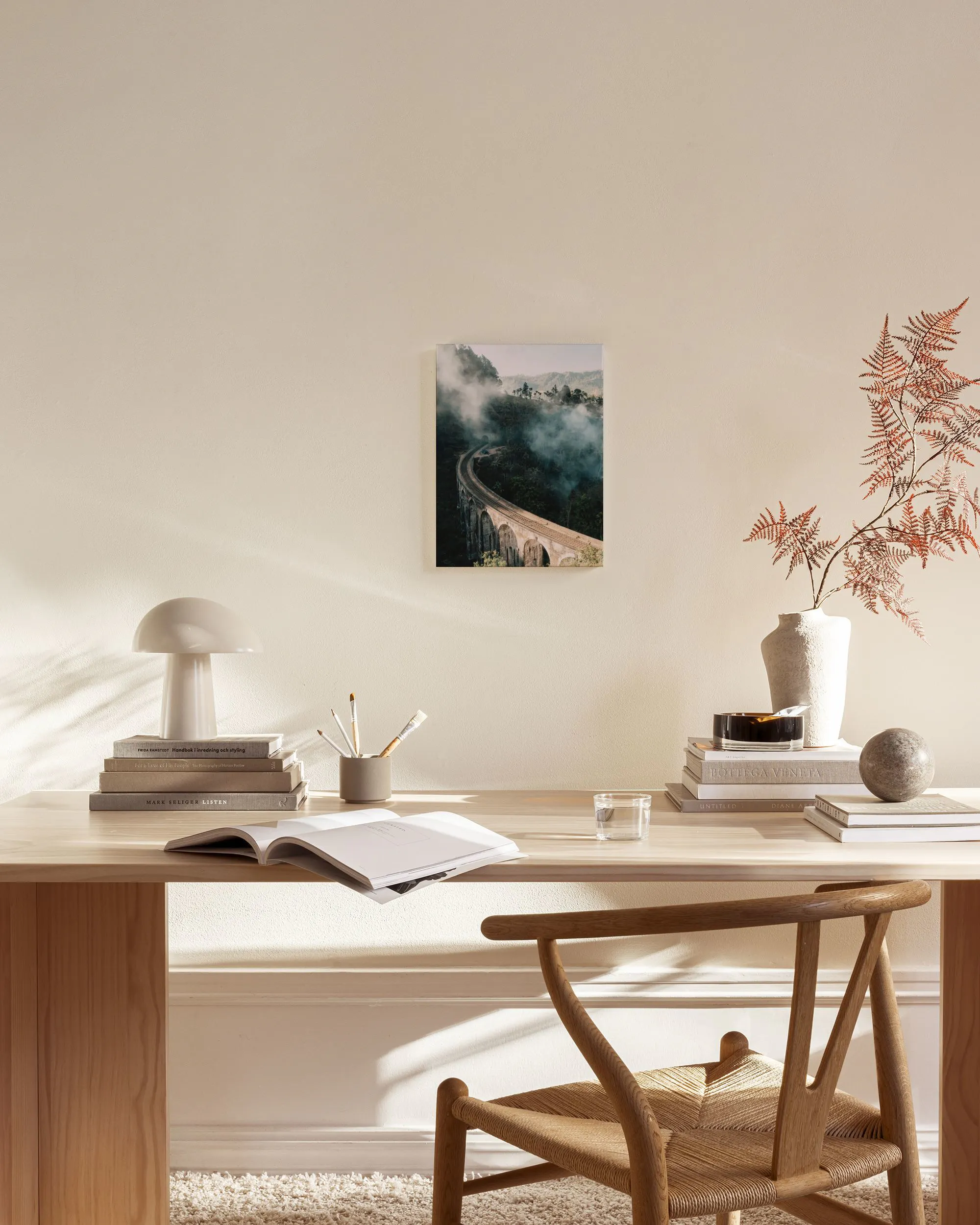 Toile dun pont en pierre dans une vallée brumeuse, accrochée dans un salon lumineux avec un fauteuil en bois.
