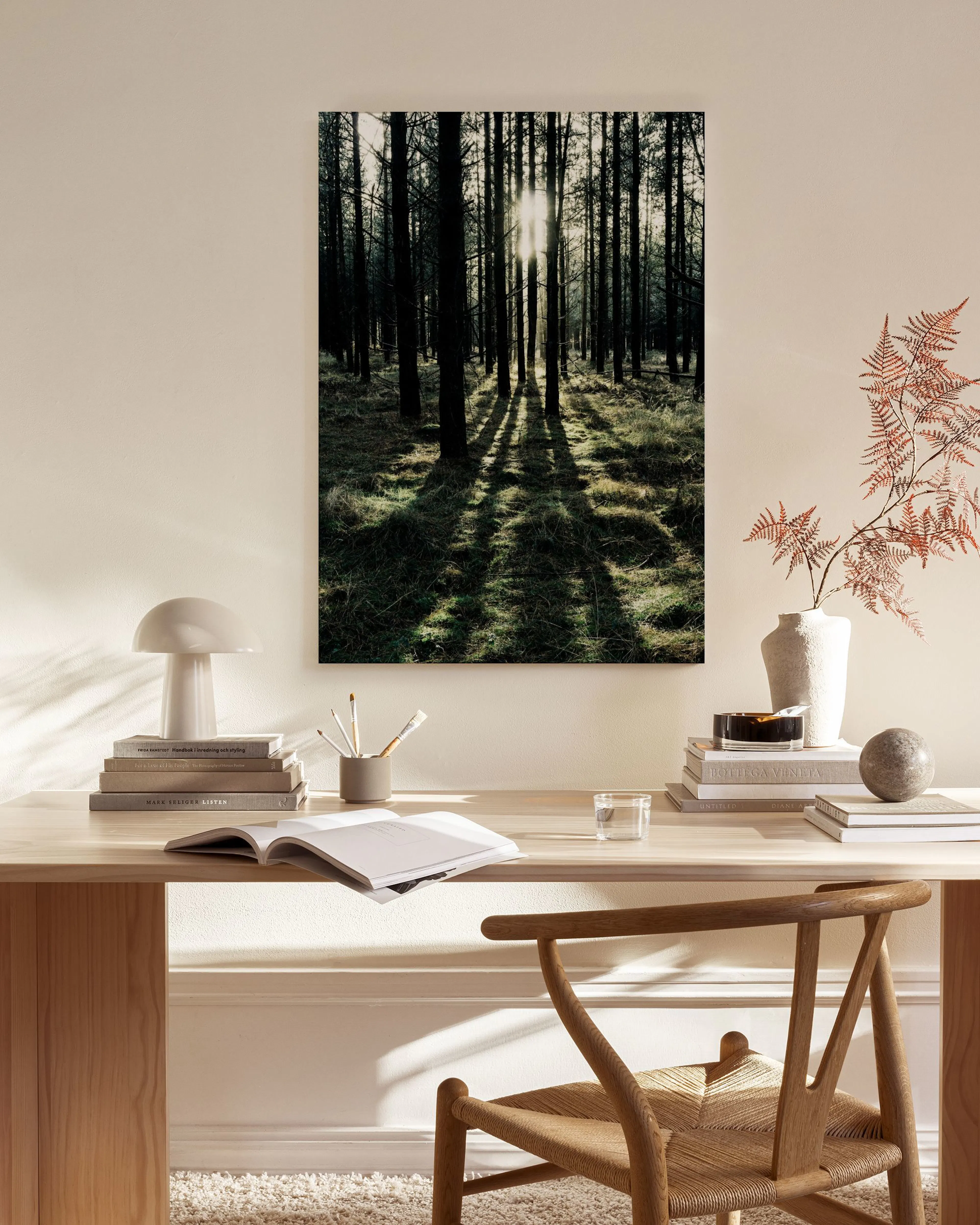 Lerretsbilde av en skog med mørke trestammer og sollys som skinner gjennom, henger i en lys stue.