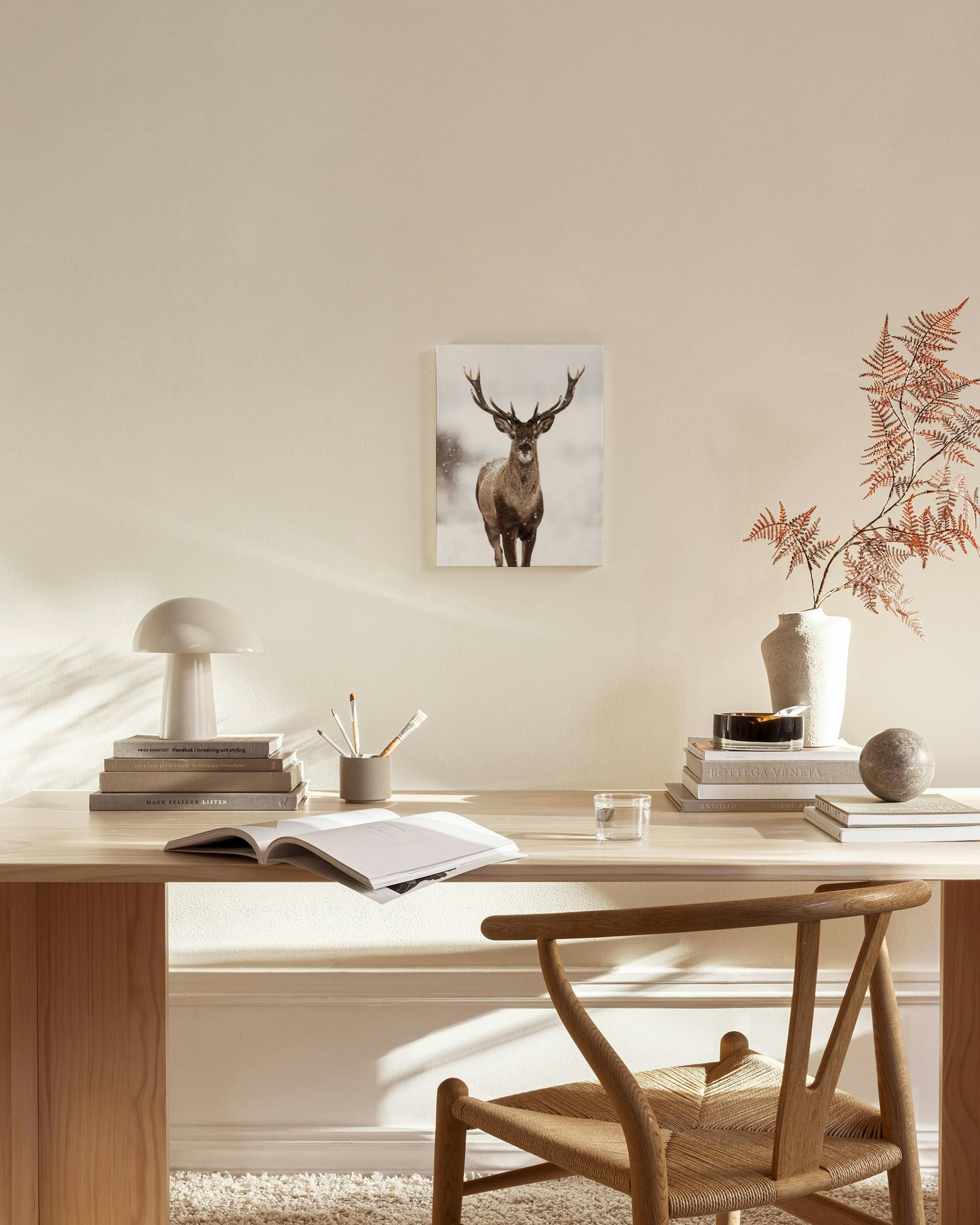 A canvas print of a majestic deer in a snowy landscape, hanging above a wooden console table in a minimalist living room.