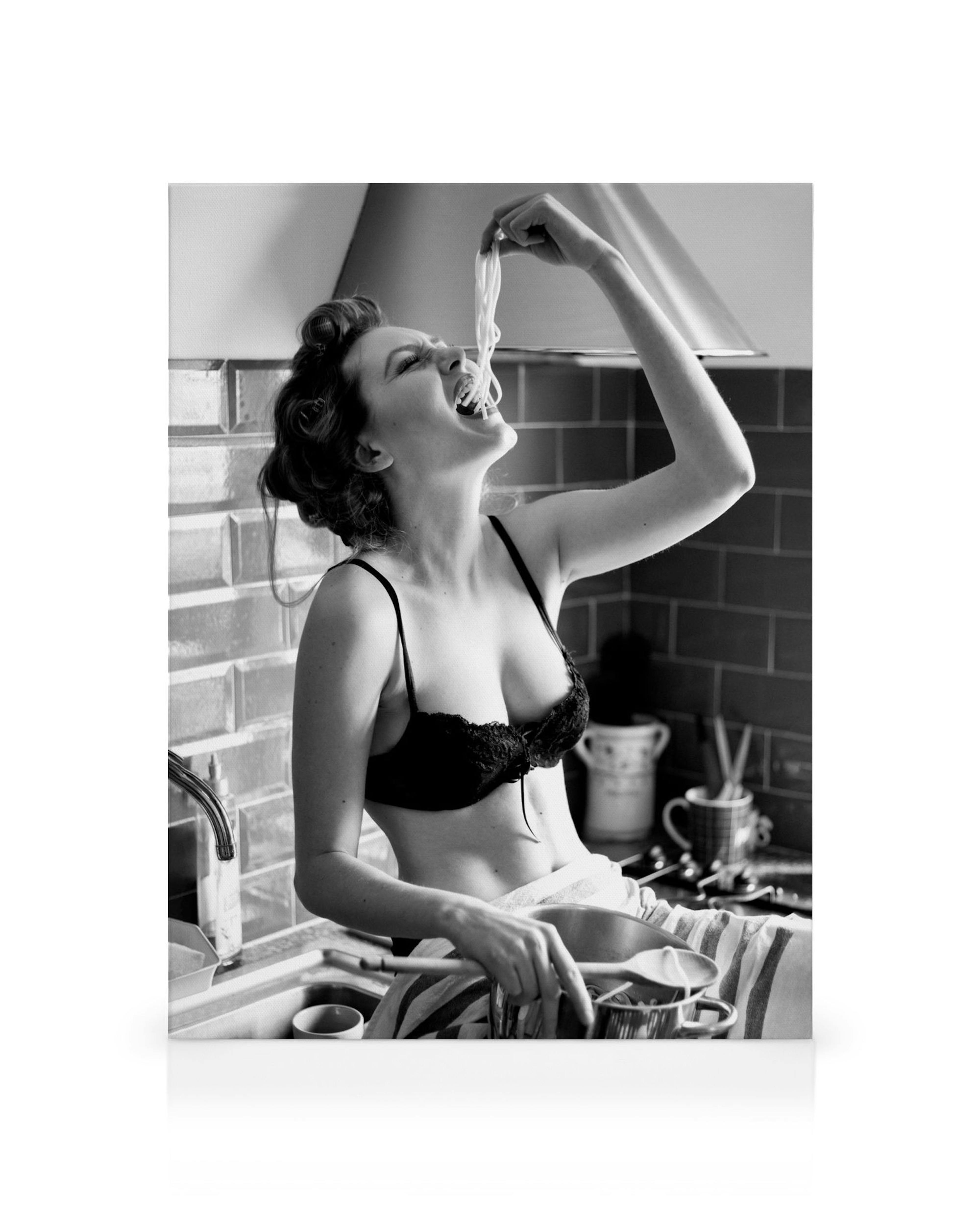 Schwarz-Weiß-Leinwandbild einer jungen Frau in Dessous, die genüsslich Spaghetti aus einem Topf isst. Küchendarstellung, Pasta-M