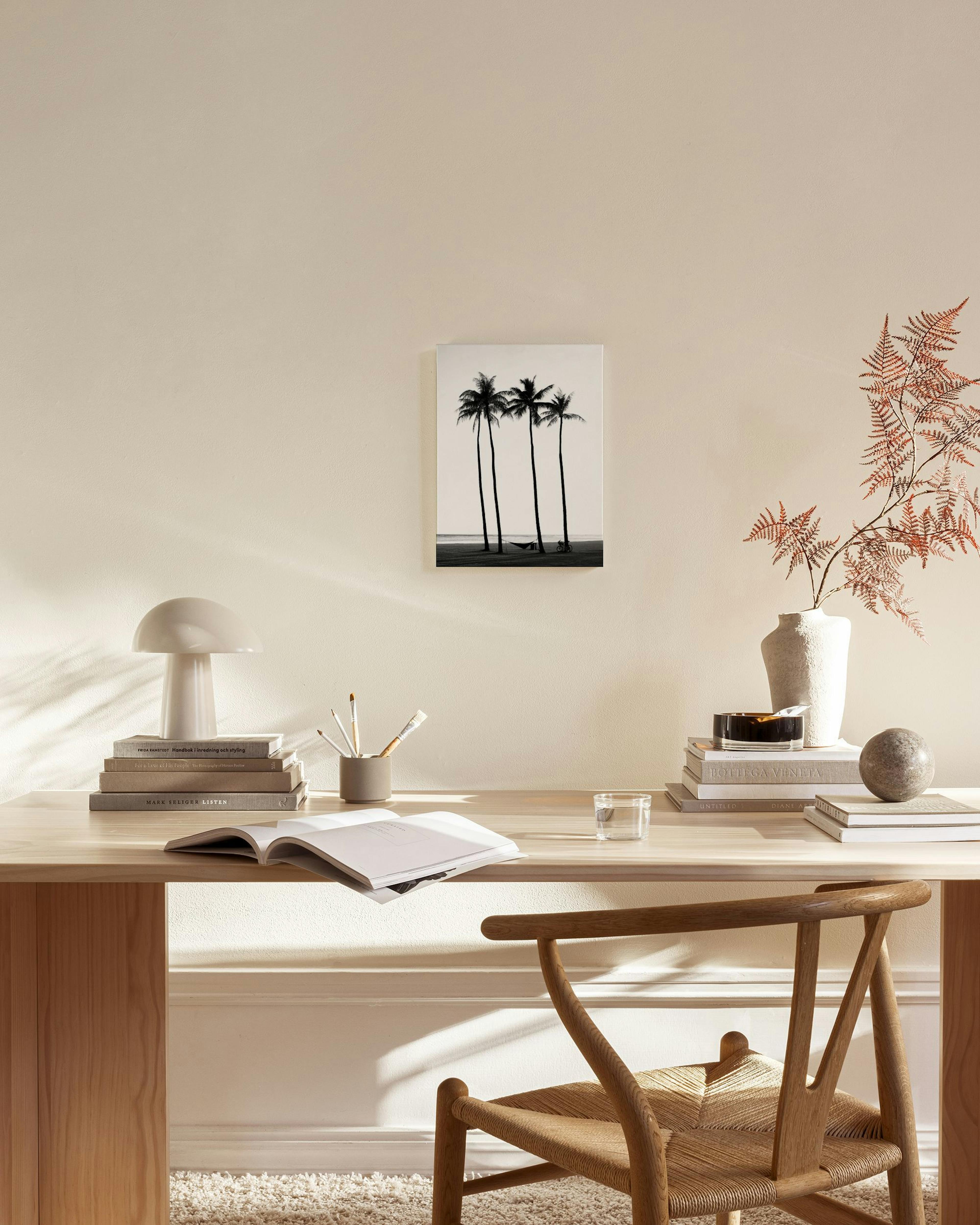 A monochrome palm tree print on a wall in a neutral living room with a wooden chair and coffee table.