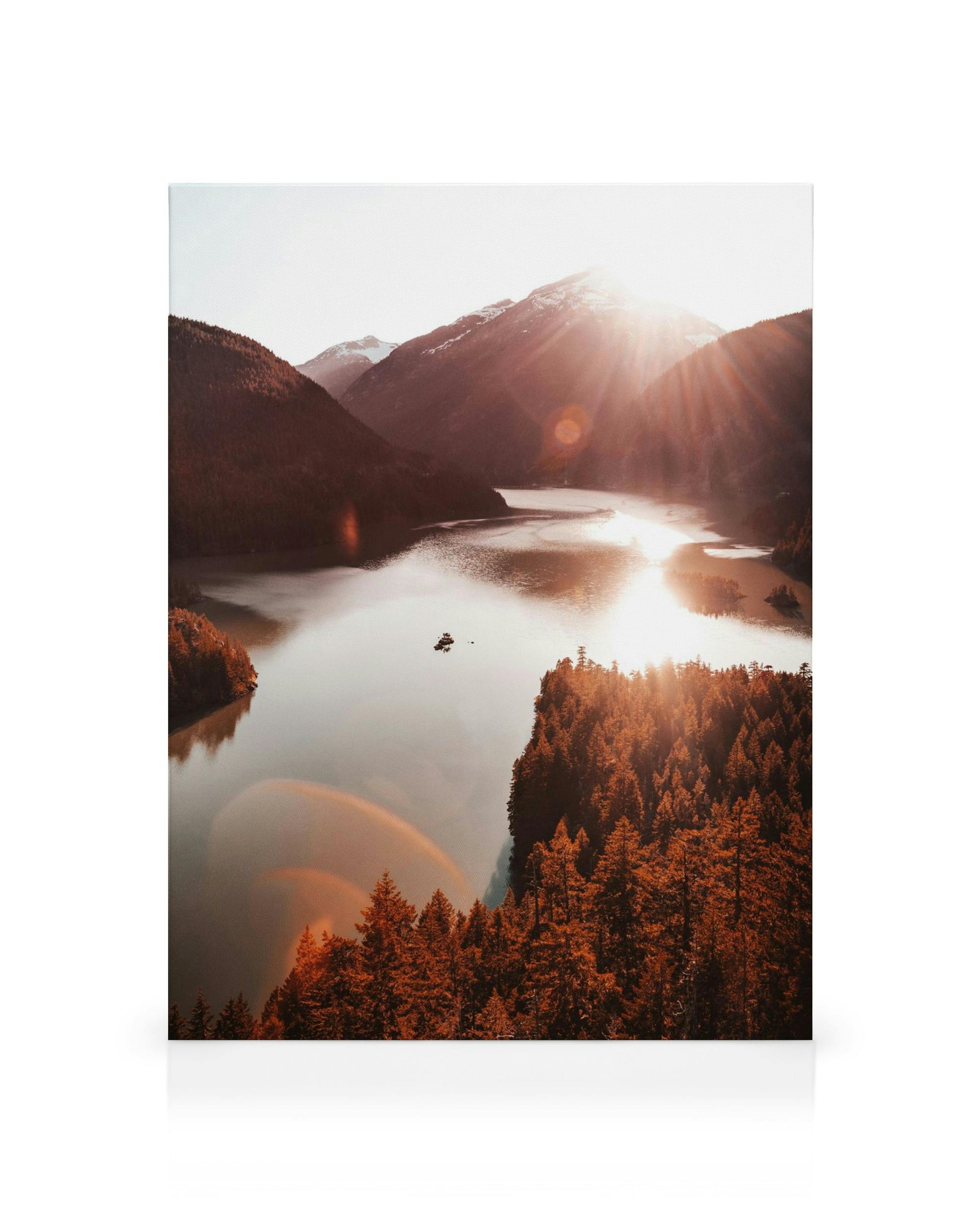 Photograph of Diablo Lake at sunset with red-orange trees and mountains, sunbeams reflecting on the water.