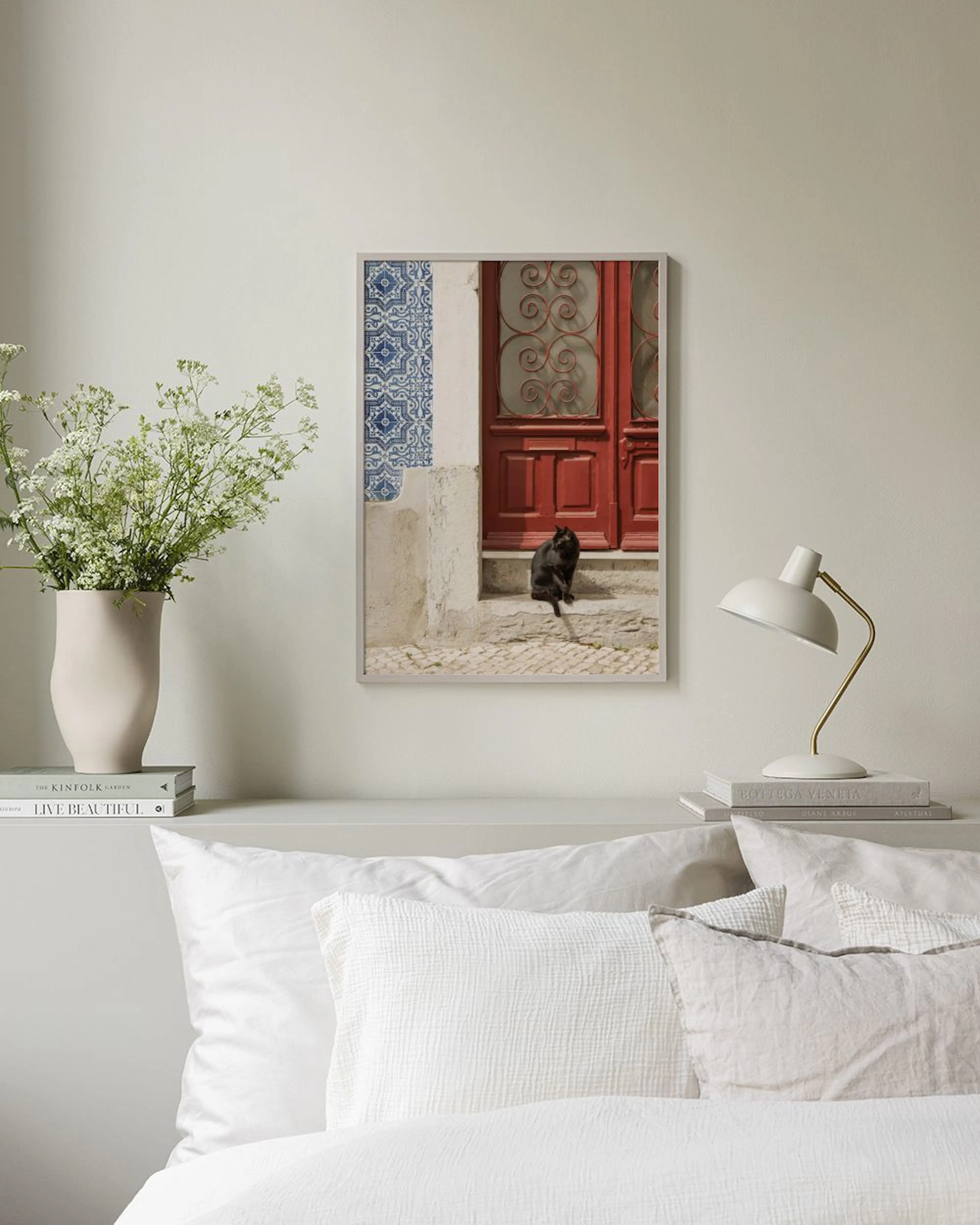 Póster de un gato negro frente a una puerta roja y azulejos azules, colgado sobre una mesa de madera con desayuno.