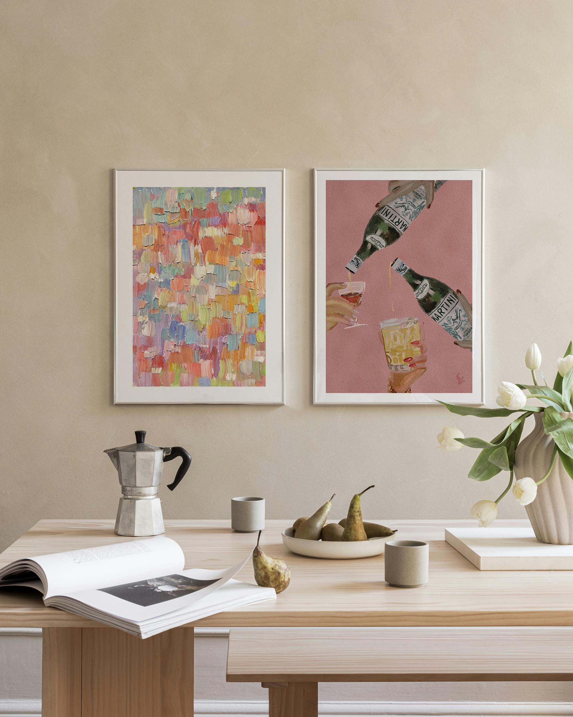 Twee postersets aan een muur boven een houten tafel met een koffiepot, peren en een boek.