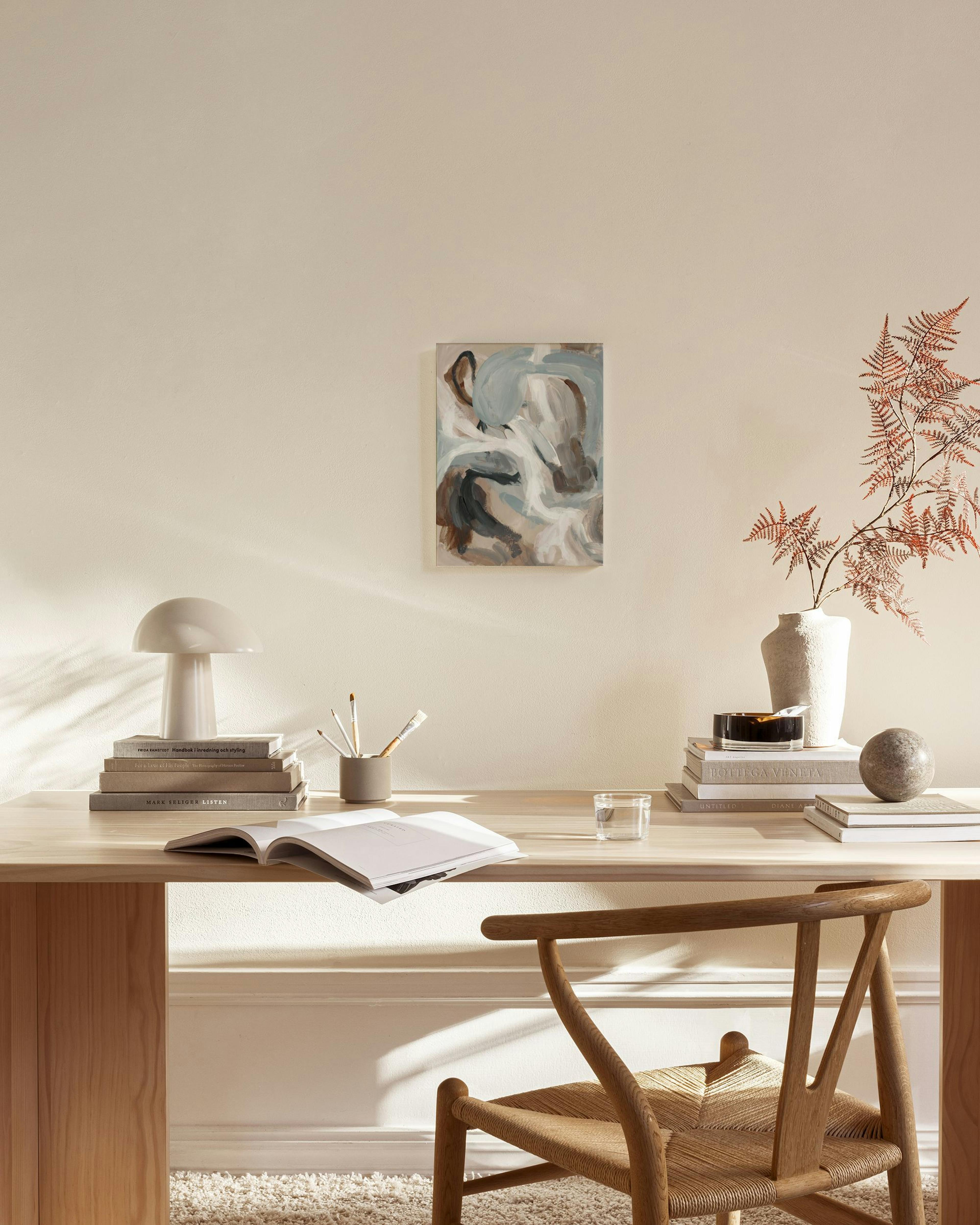 Toile abstraite aux formes organiques gris-bleu, marron et blanc, accrochée dans un salon clair au-dessus dun banc en bois.