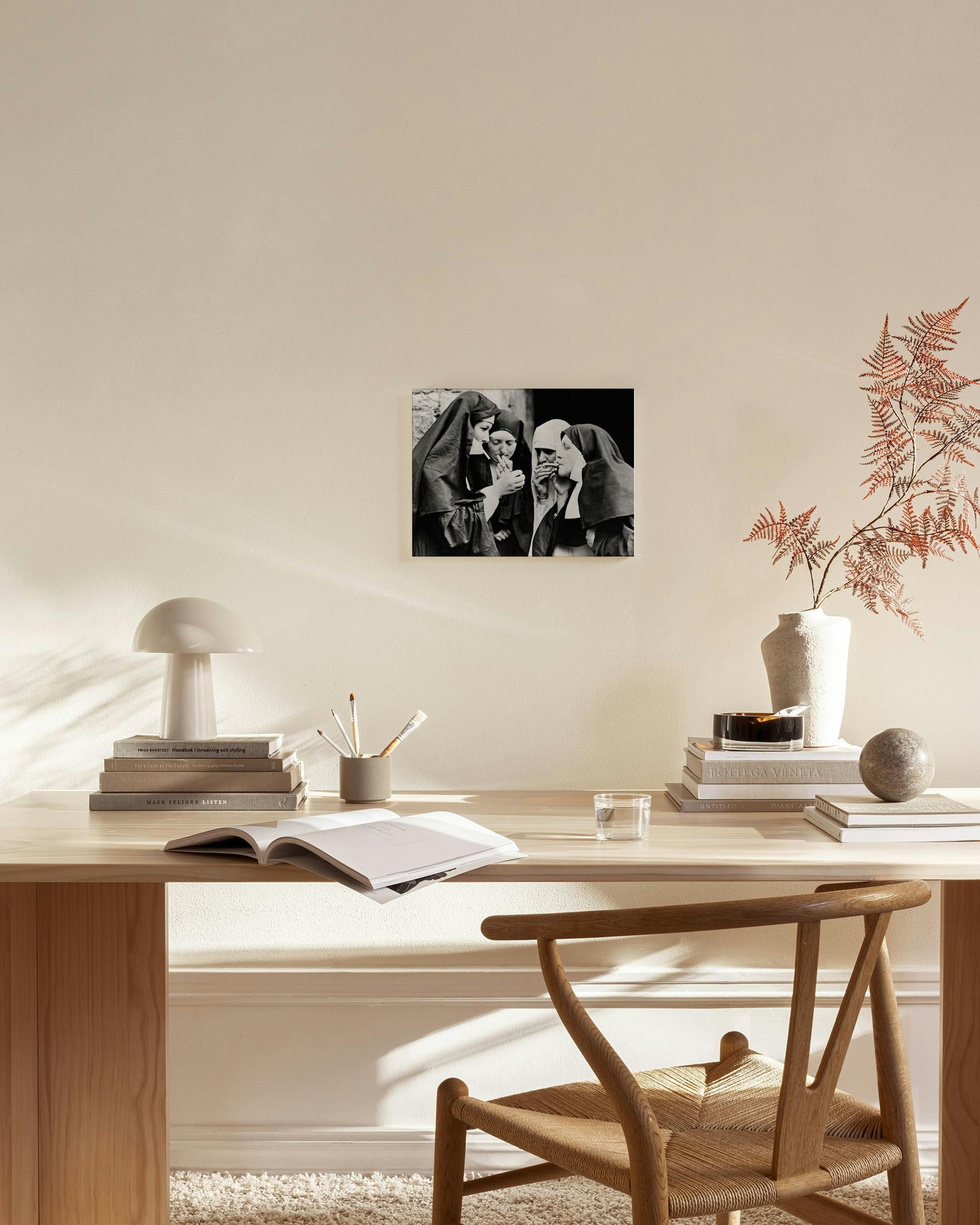 A black and white canvas print depicting four nuns, hanging on a cream wall above a timber console table in a minimalist living 
