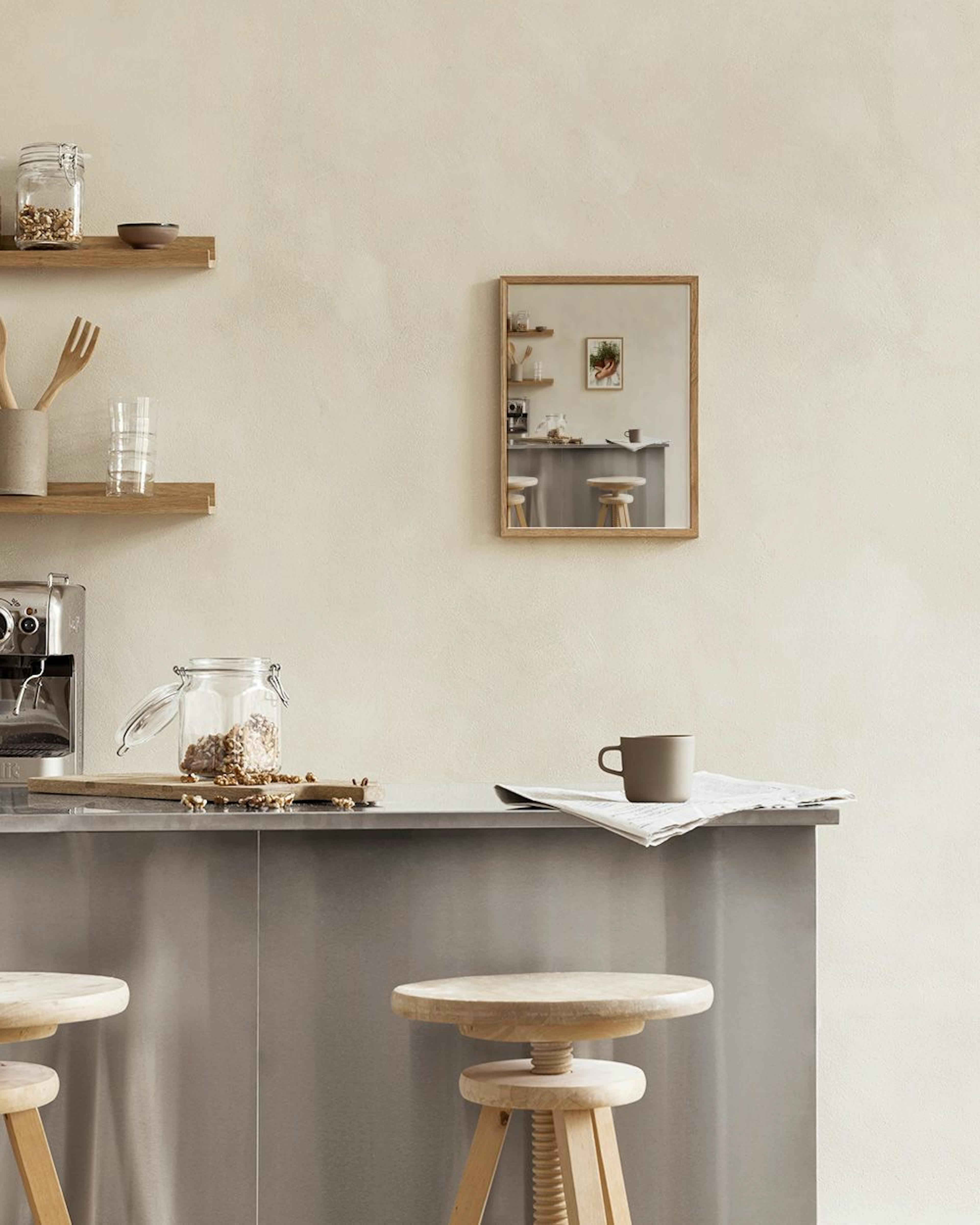 A print of hands holding a pot of rosemary, displayed in a rustic kitchen above a metal counter with wooden stools.
