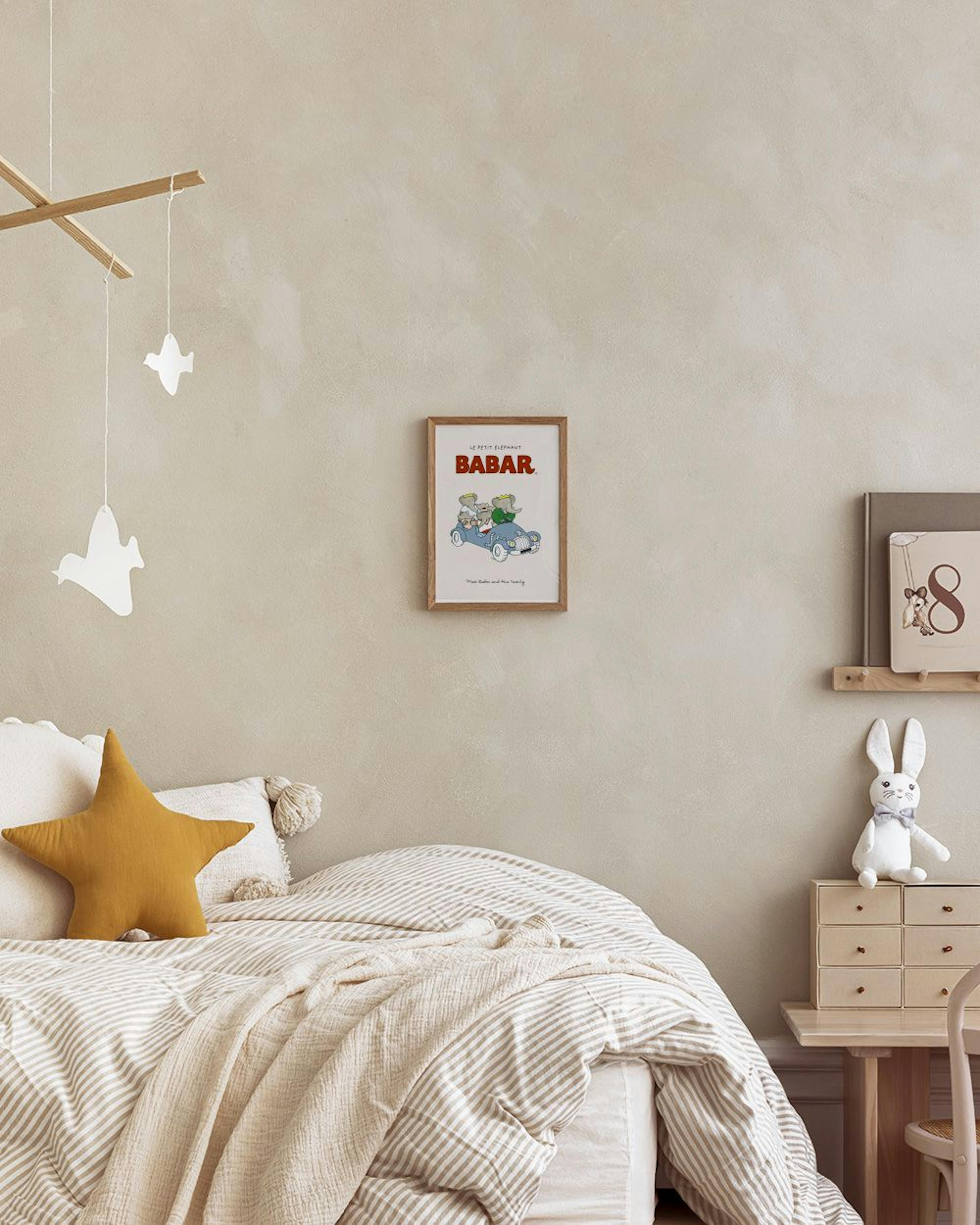 Affiche Babar avec trois éléphants en voiture bleue, suspendue au-dessus dun bureau en bois dans une chambre denfant.