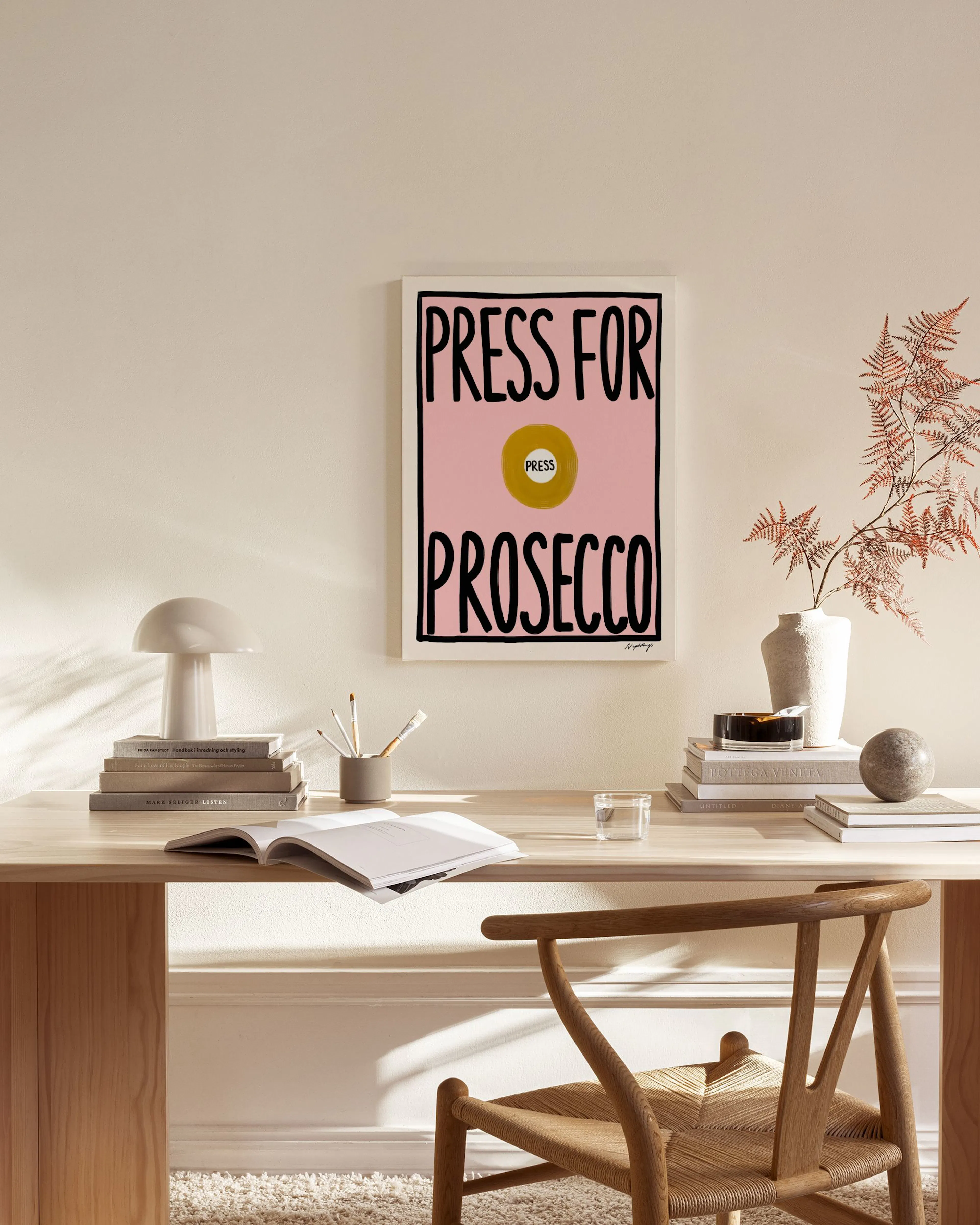 Canvastavla med texten PRESS FOR PROSECCO i svart på rosa bakgrund, hängande i ett ljust vardagsrum.