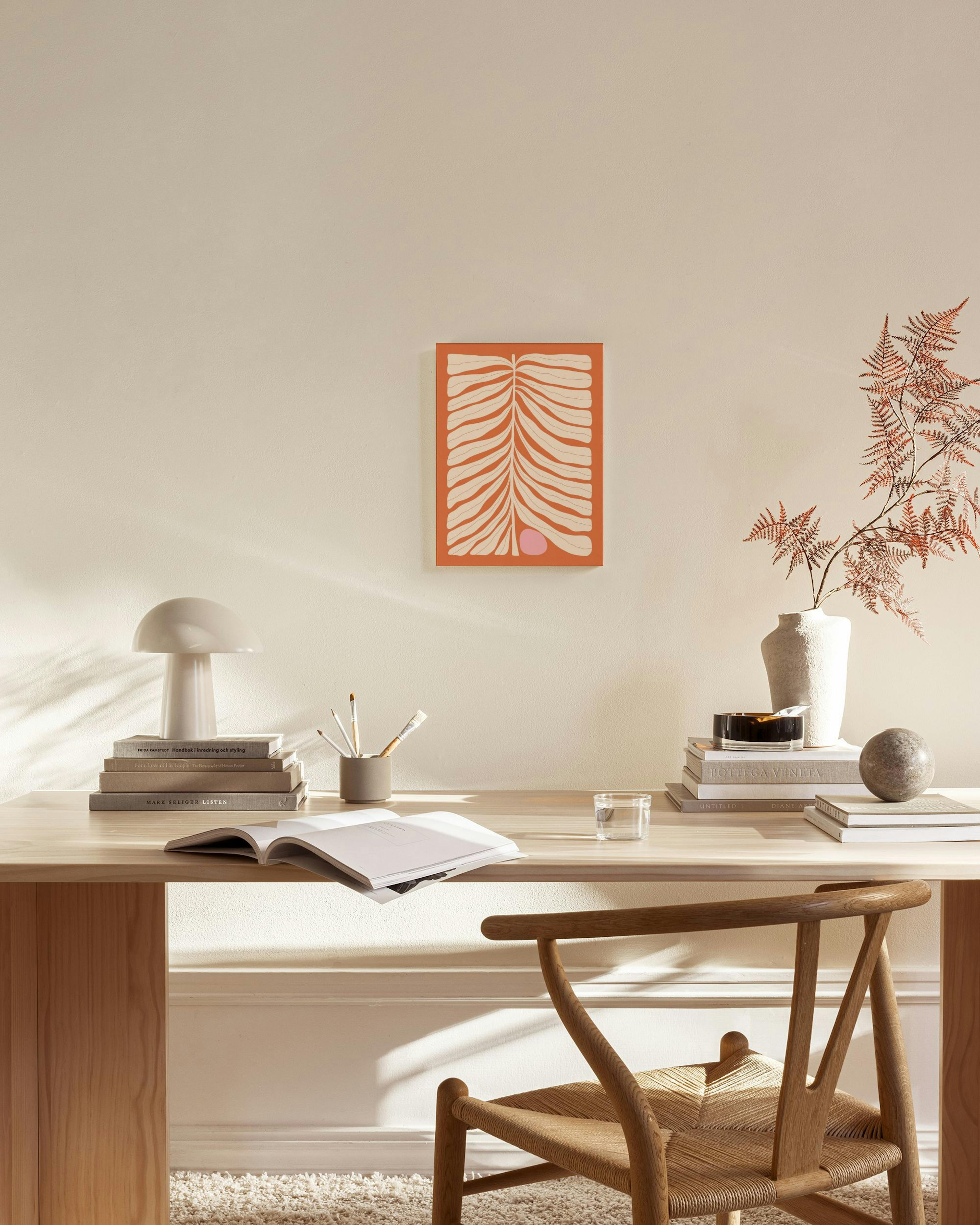 Canvastavla med orange bakgrund och beiga bladmönster, hängande i ett ljust vardagsrum ovanför en bänk.