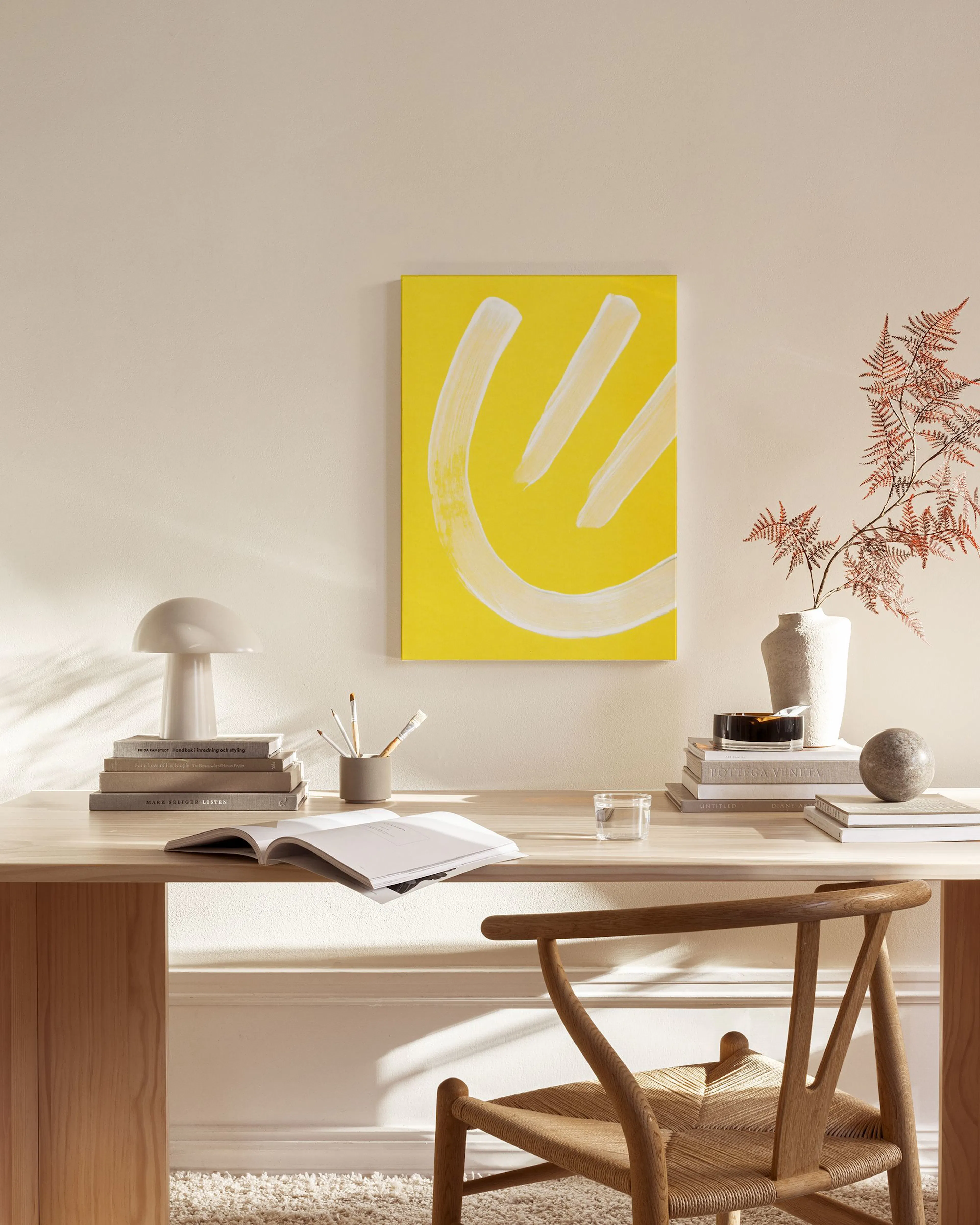 Yellow canvas print with white brushstrokes forming a curved shape and two short lines, displayed in a bright living room.