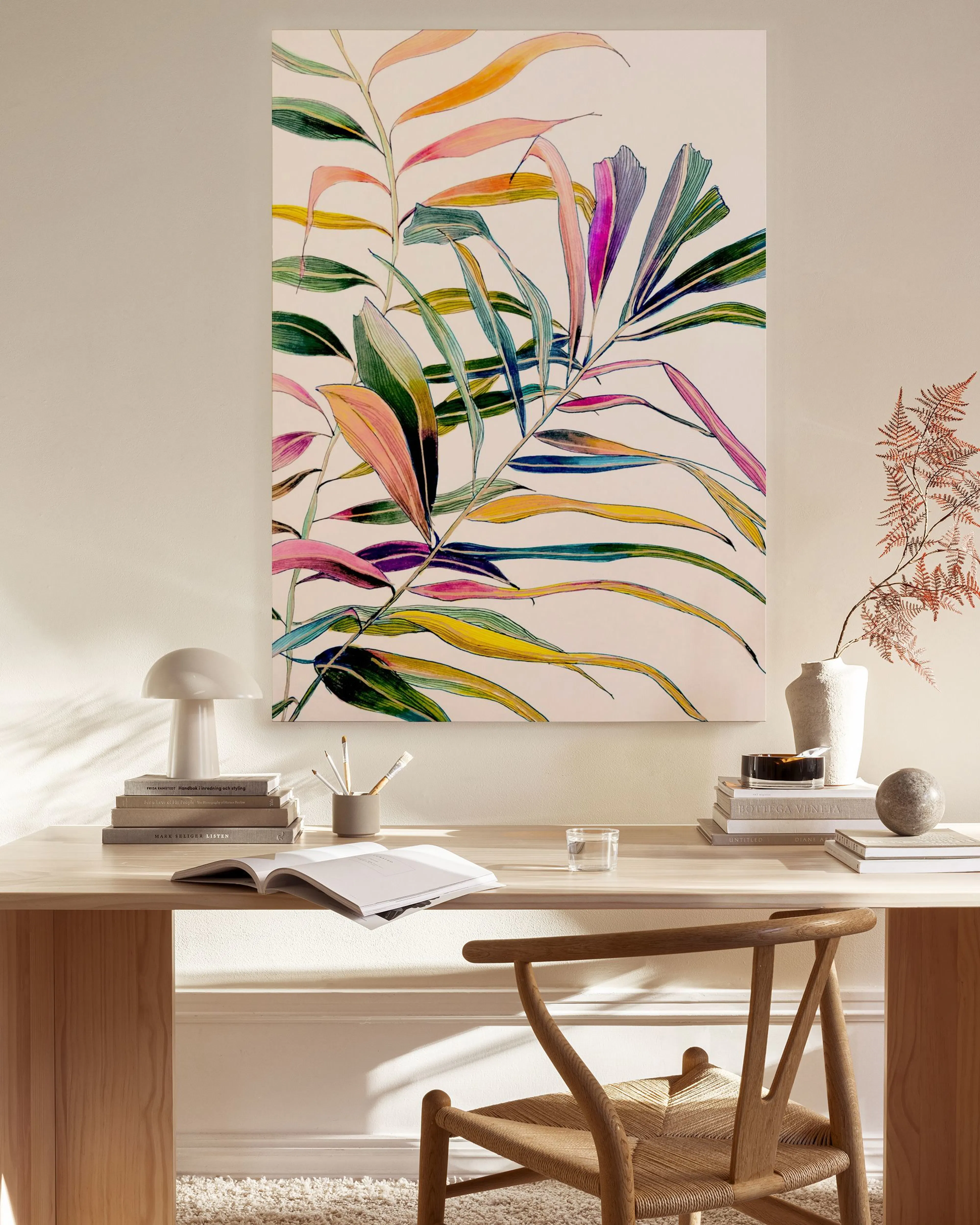 Lienzo con hojas tropicales de colores vibrantes, colgado sobre un mueble auxiliar de madera junto a un sillón y mesa de centro.