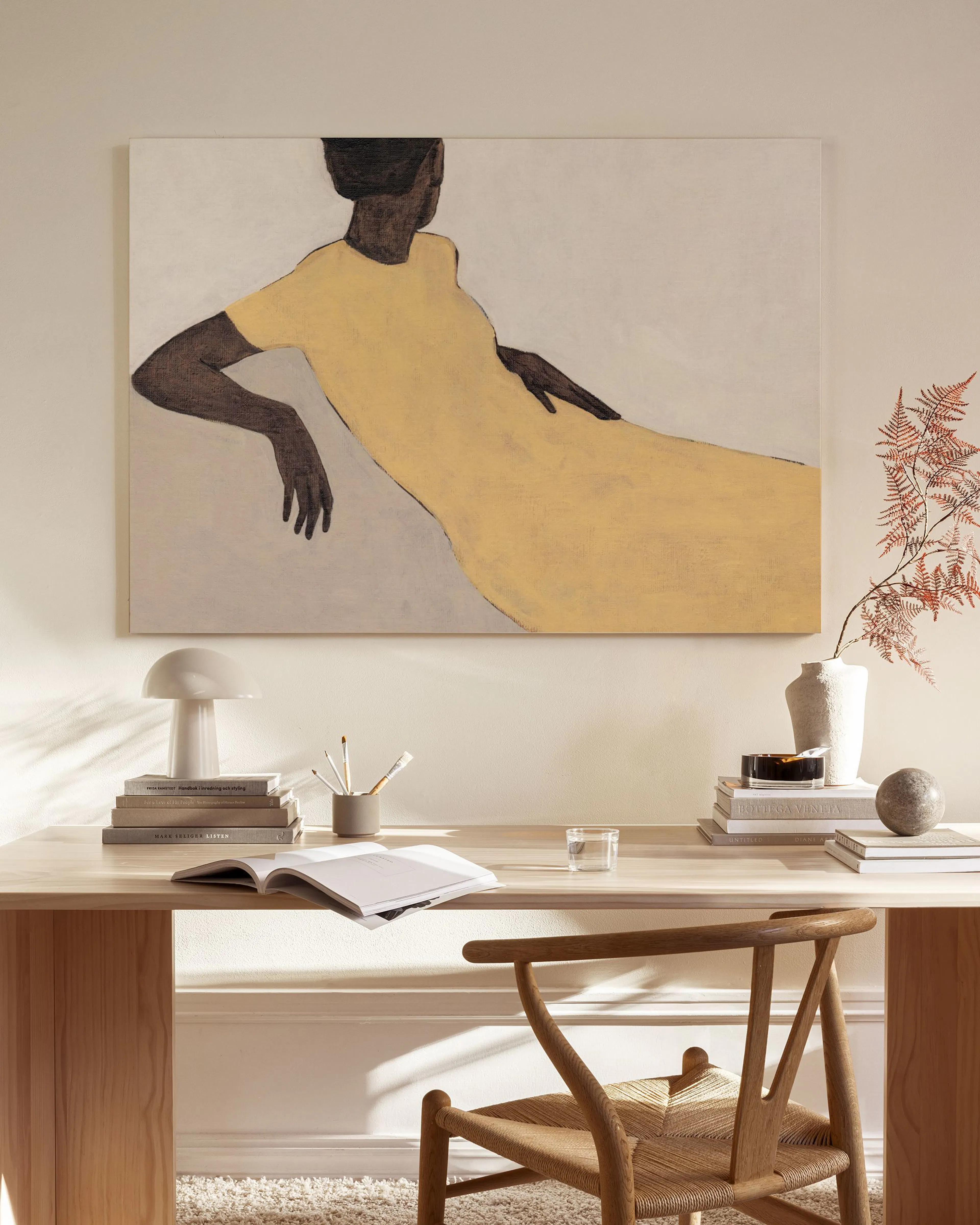 A canvas print of a woman in a yellow dress, seated, displayed above a wooden console table in a minimalist living room.