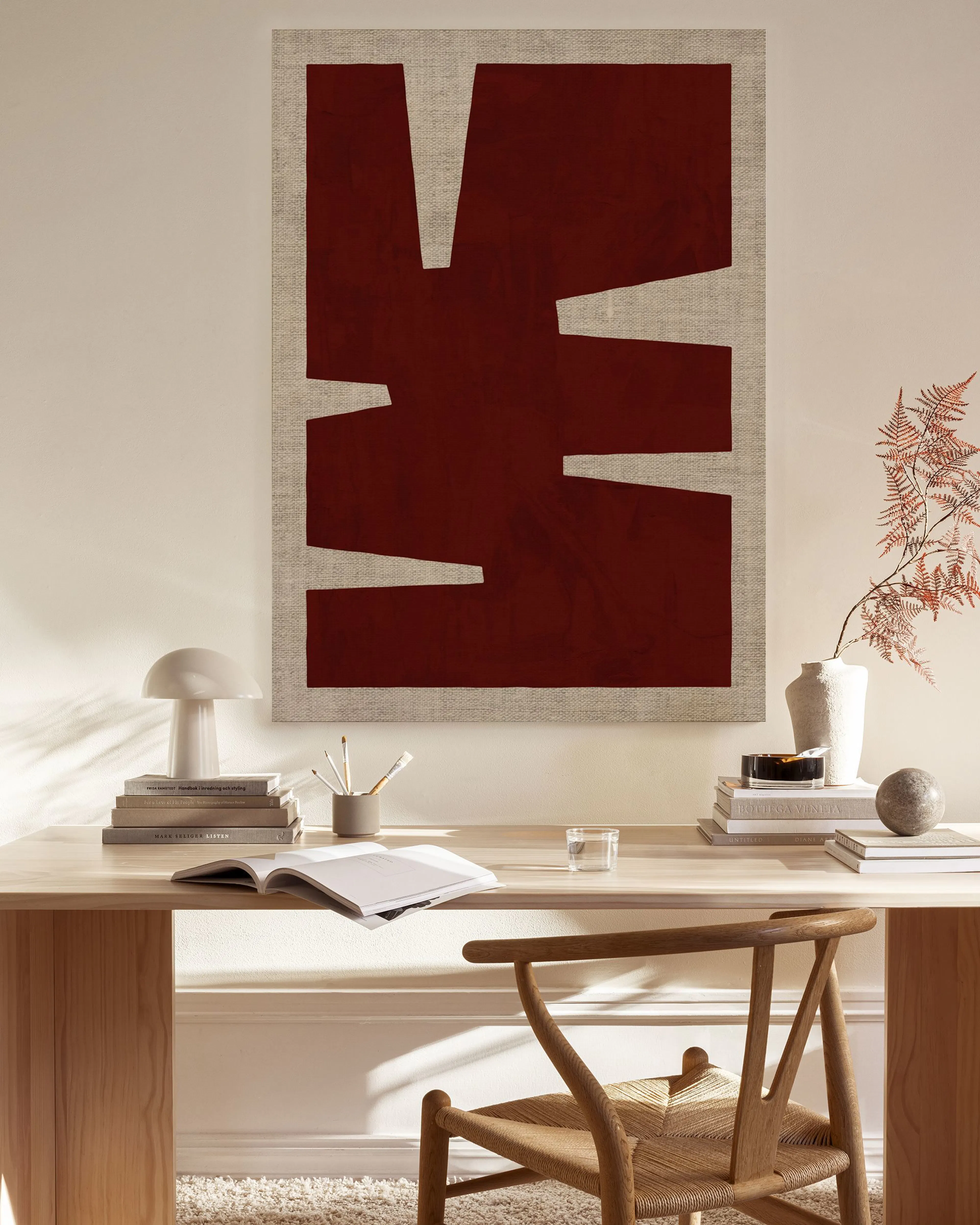 A deep red abstract canvas print with irregular shapes on a light background, hanging above a console table in a minimalist livi