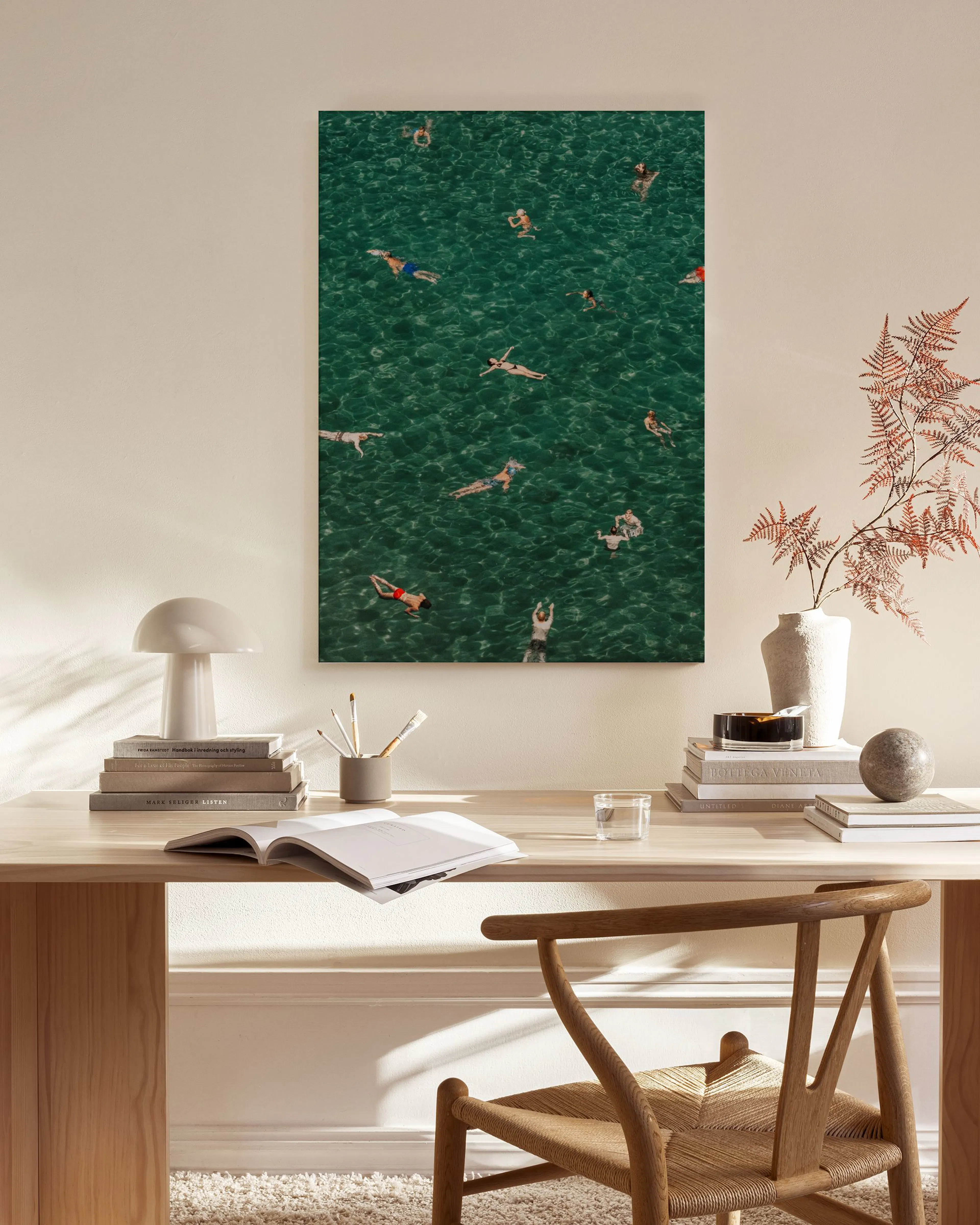Toile de personnes nageant dans une eau vert émeraude, accrochée au-dessus dun meuble bas en bois dans un salon moderne.