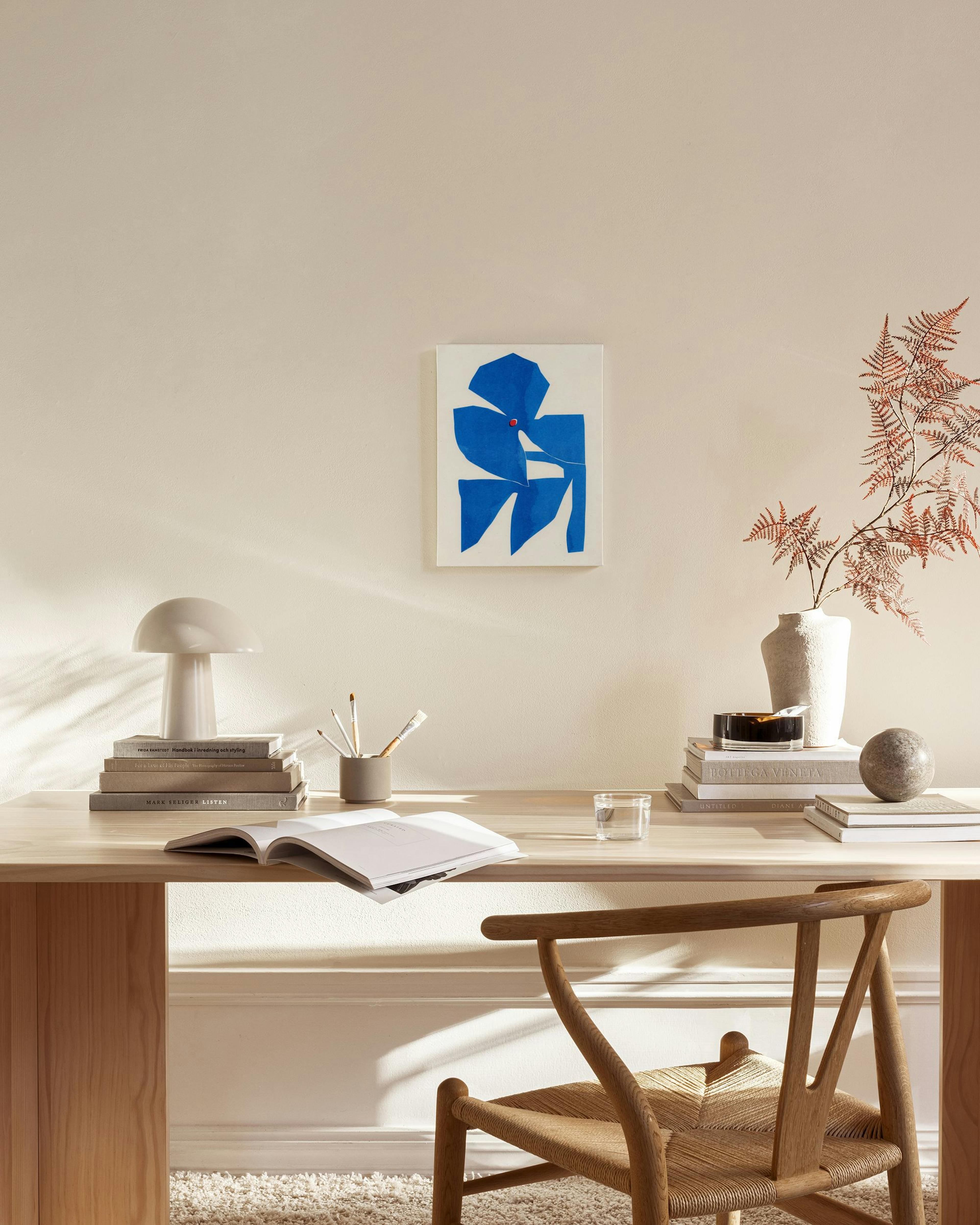Abstract canvas print with bold blue shapes and a small red dot, hanging in a bright, minimalist living room.