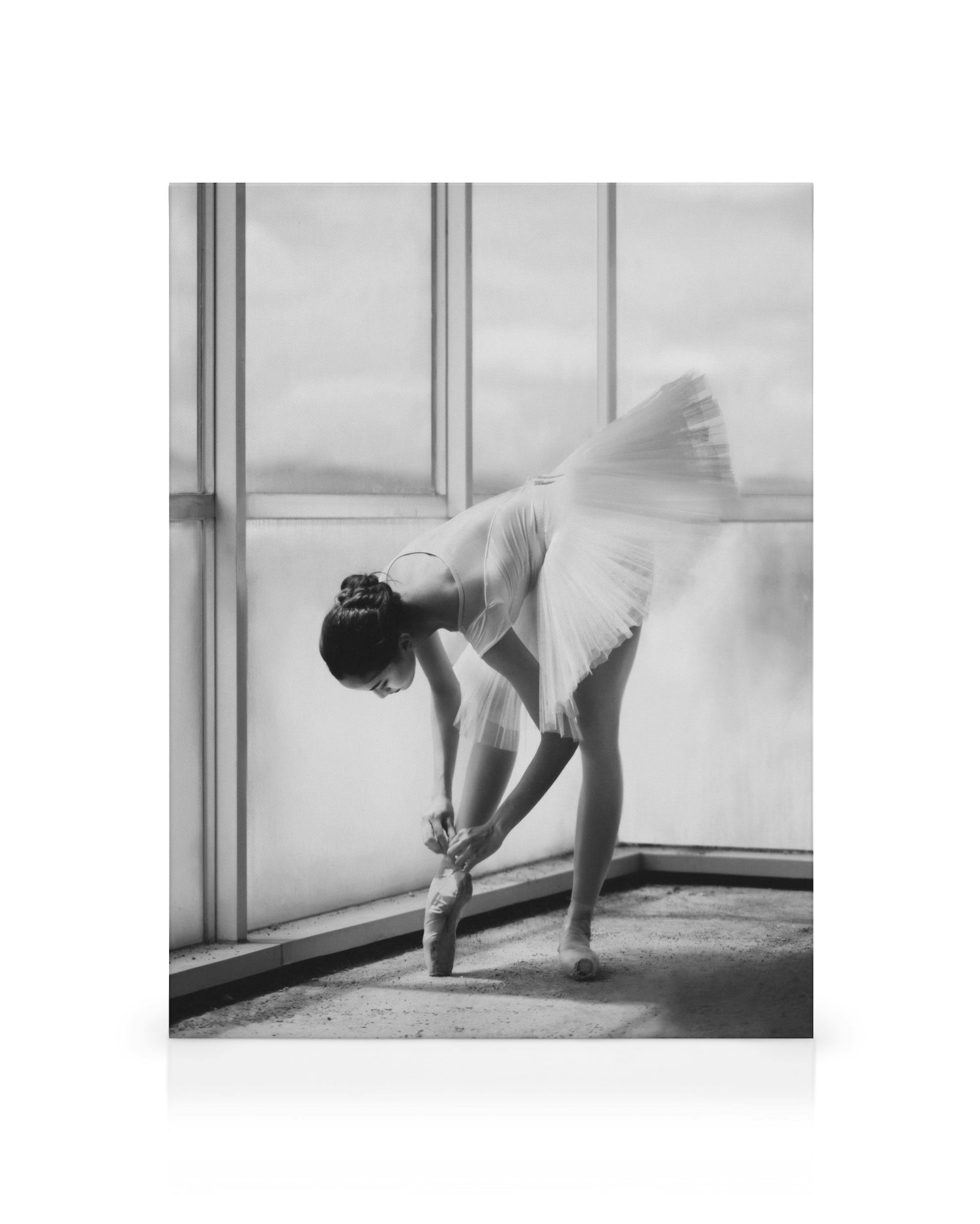 Schwarz-weißes Leinwandbild: Ballerina bindet ihre Spitzenschuhe vor einem Fenster, Fokus auf Ballett und Tanz.
