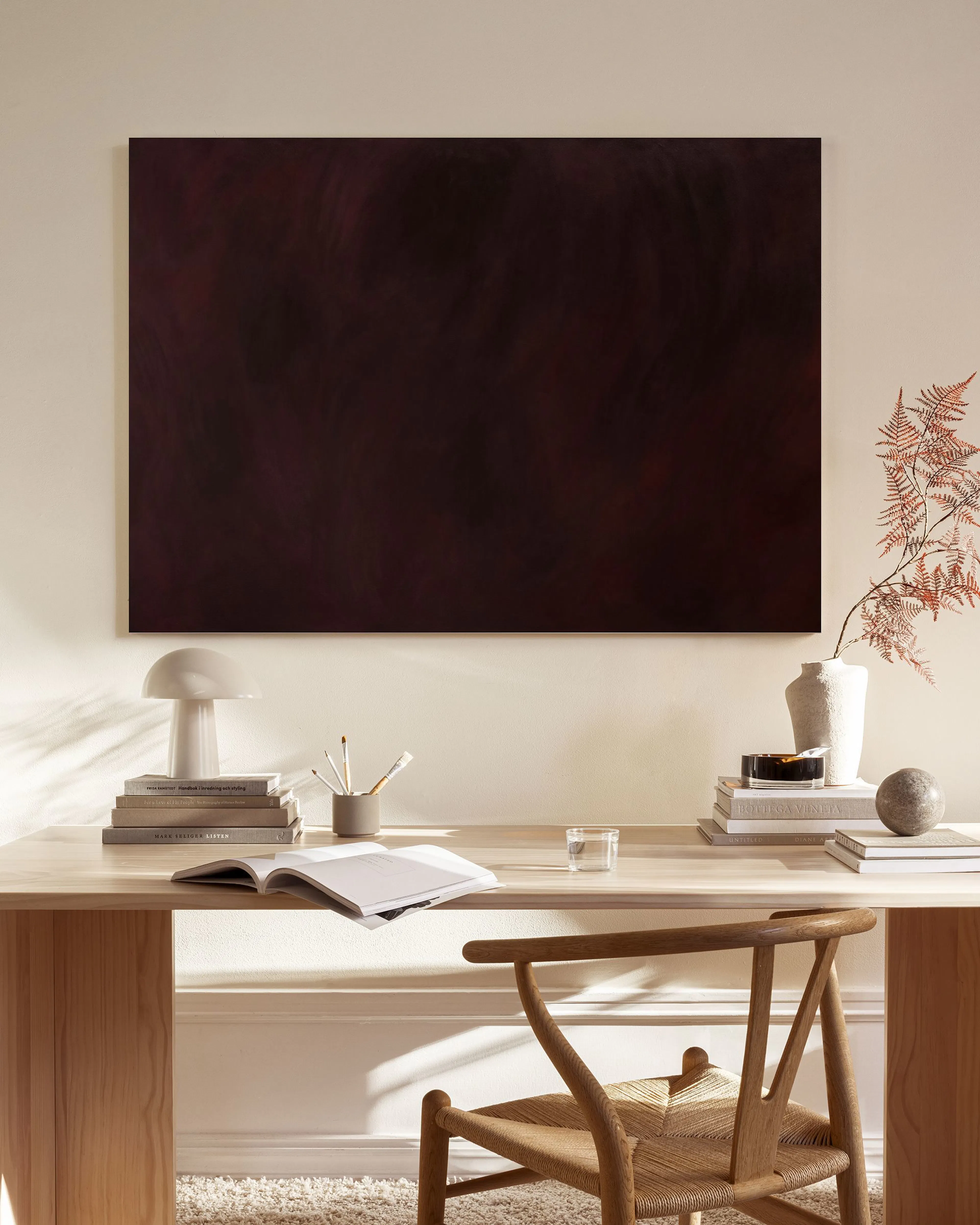 Lienzo abstracto de tonos granates y negros colgado sobre un mueble bajo, en un salón de estilo nórdico con sillón y mesa de cen