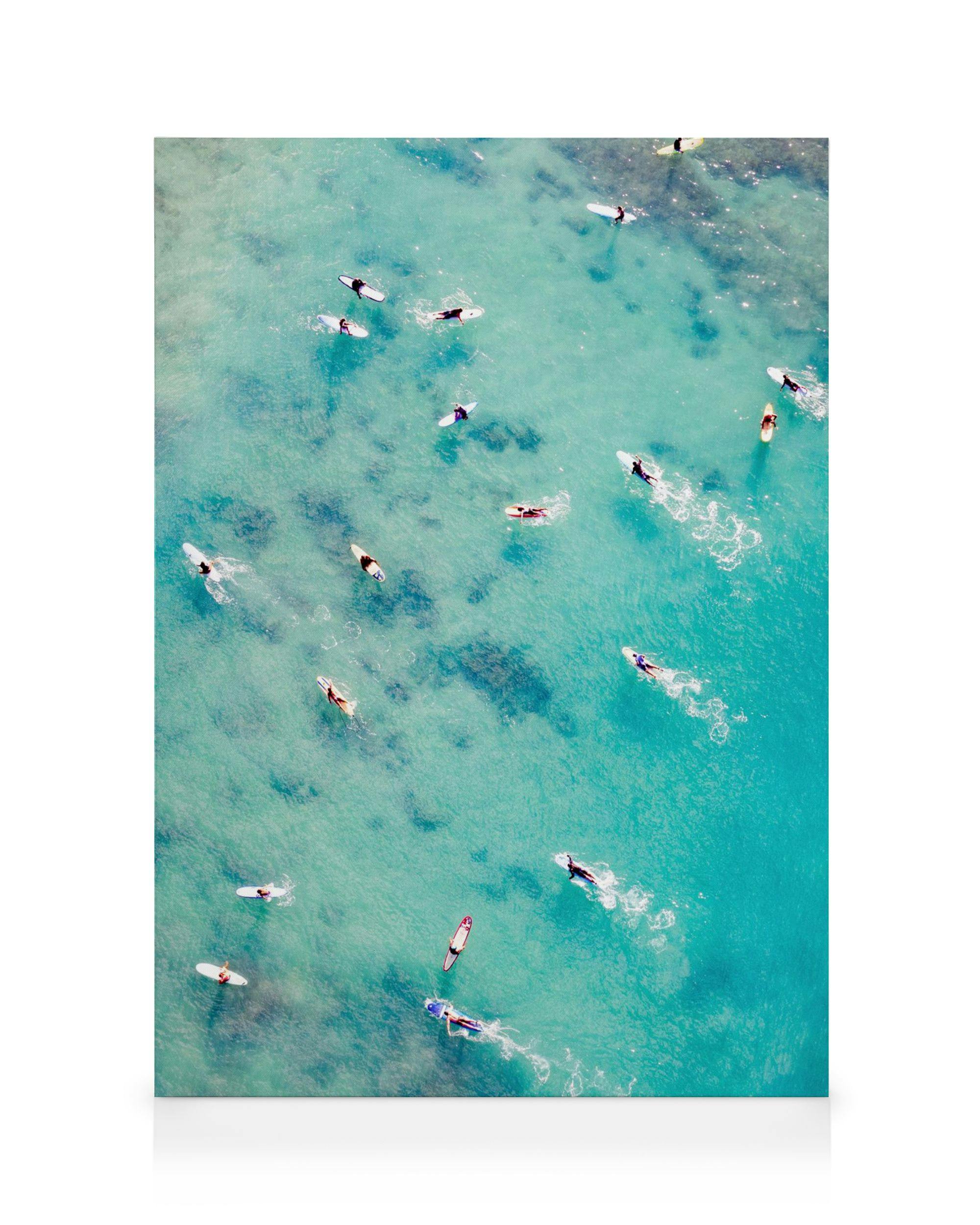A canvas print featuring an aerial view of surfers on turquoise water, with their boards and paddle strokes visible.