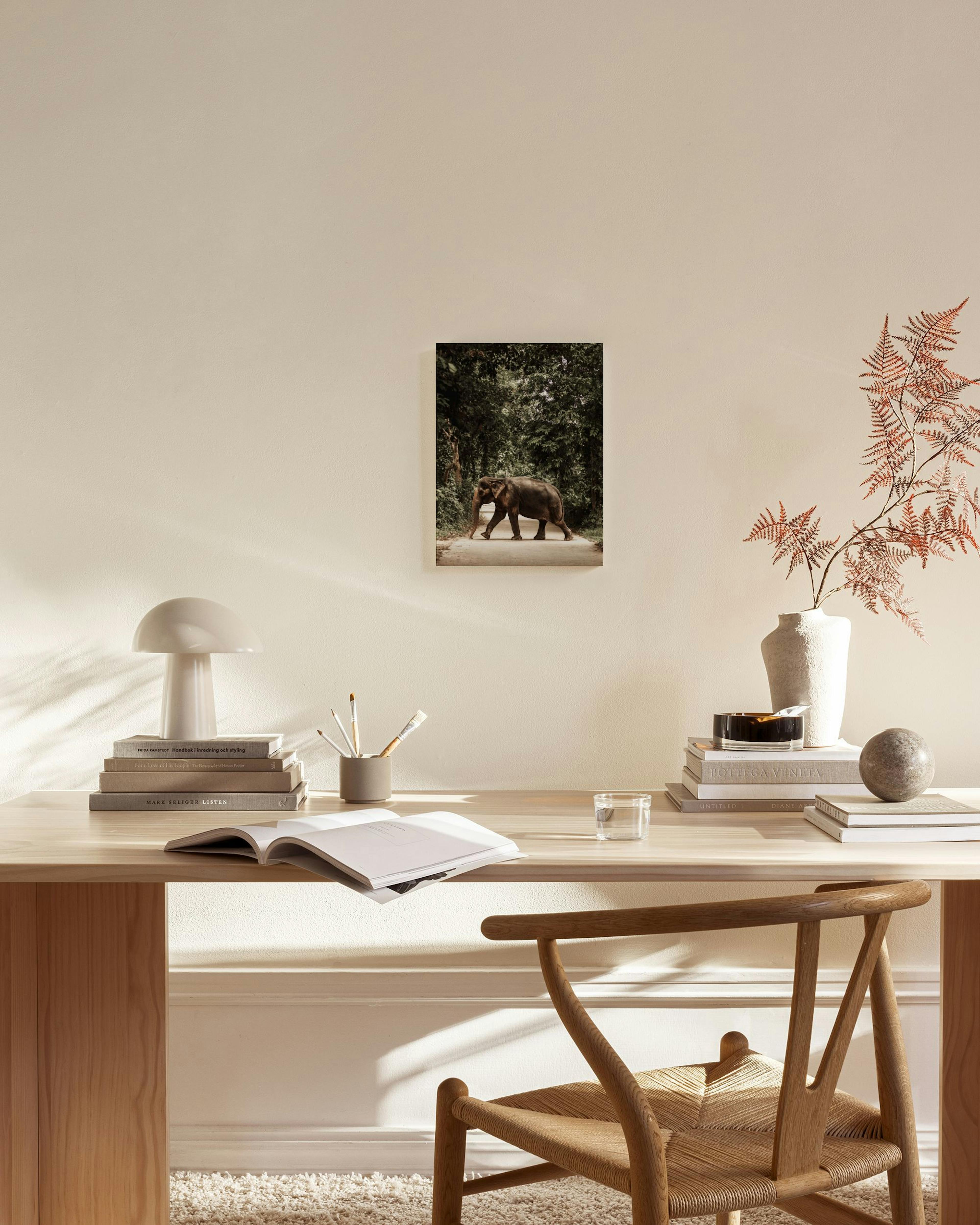 Toile dun éléphant asiatique traversant un chemin forestier, entouré dune végétation luxuriante.