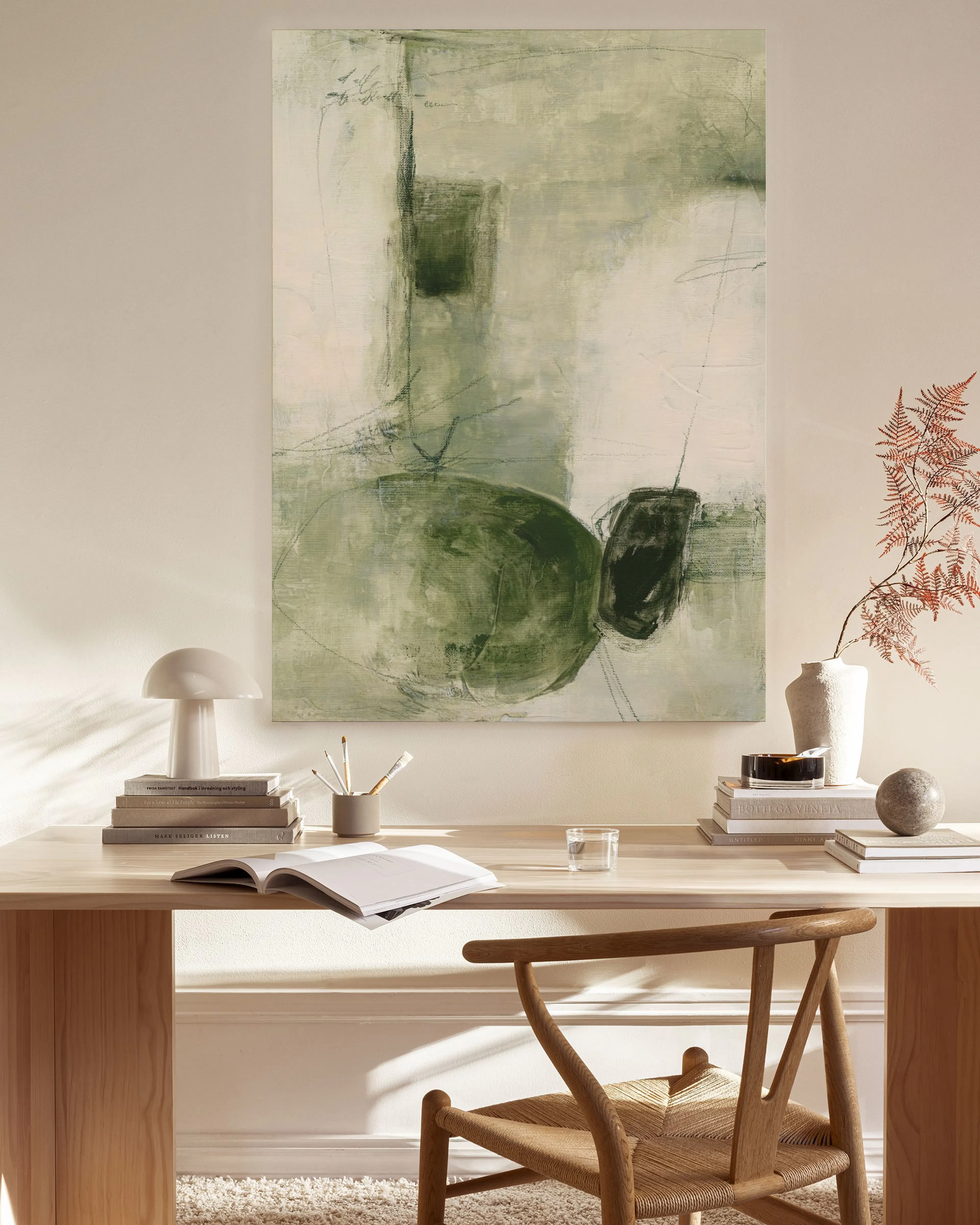 A canvas print with abstract green and grey organic shapes, displayed in a light-filled living room above a wooden console.