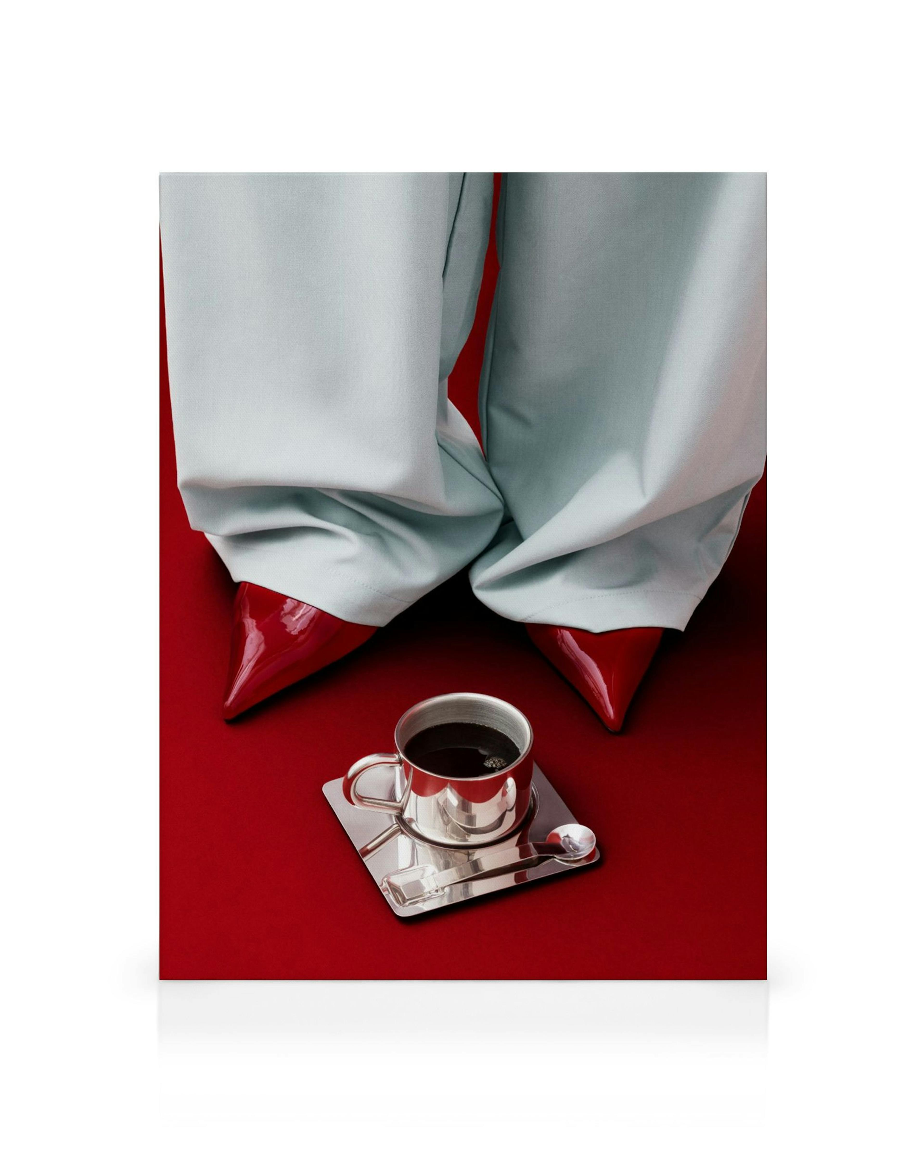 A canvas print featuring light blue pants and red pointed heels standing over a silver coffee cup on a red background.