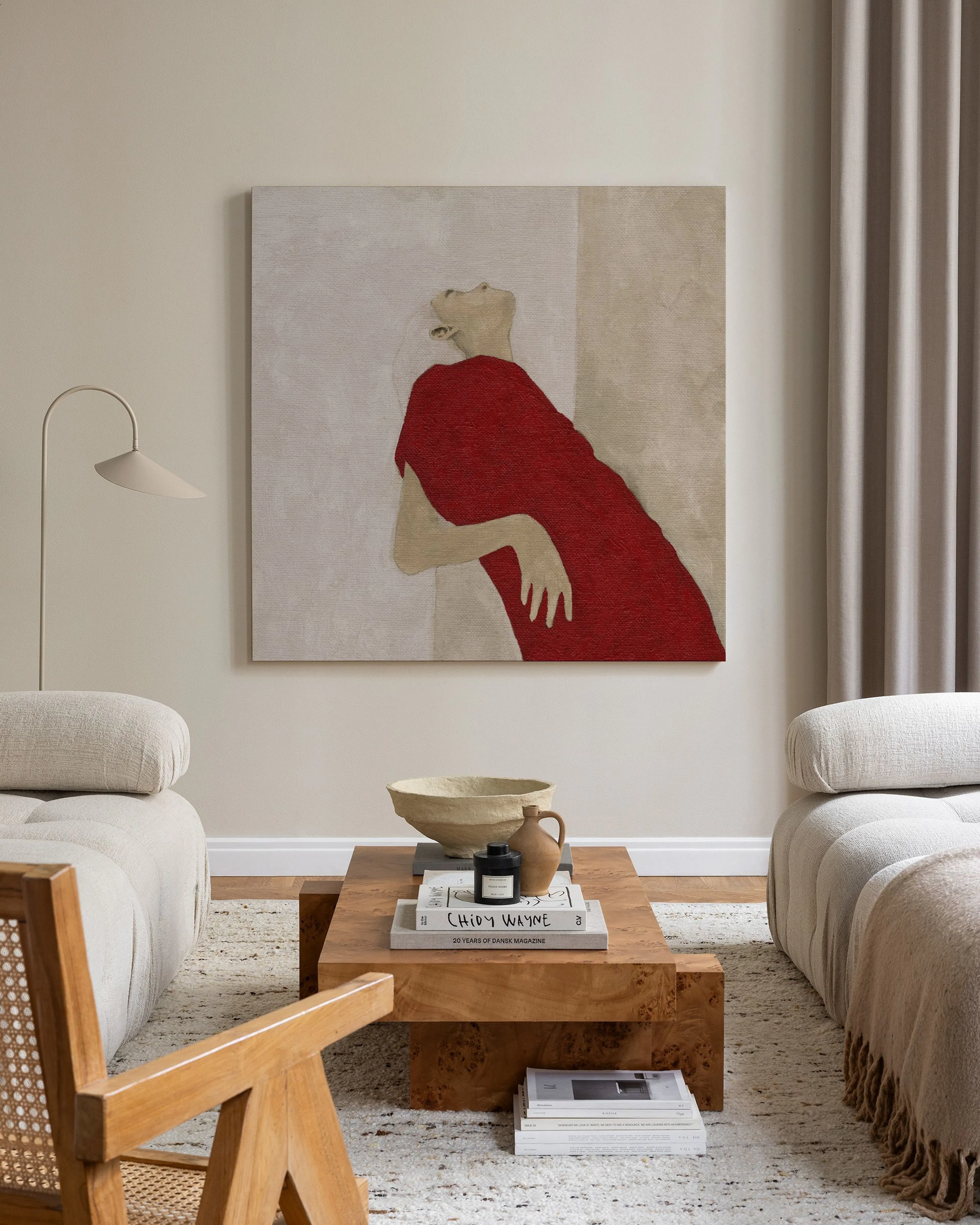 Toile murale femme en robe rouge, suspendue dans un salon moderne aux tons clairs avec fauteuil en bois et table basse.