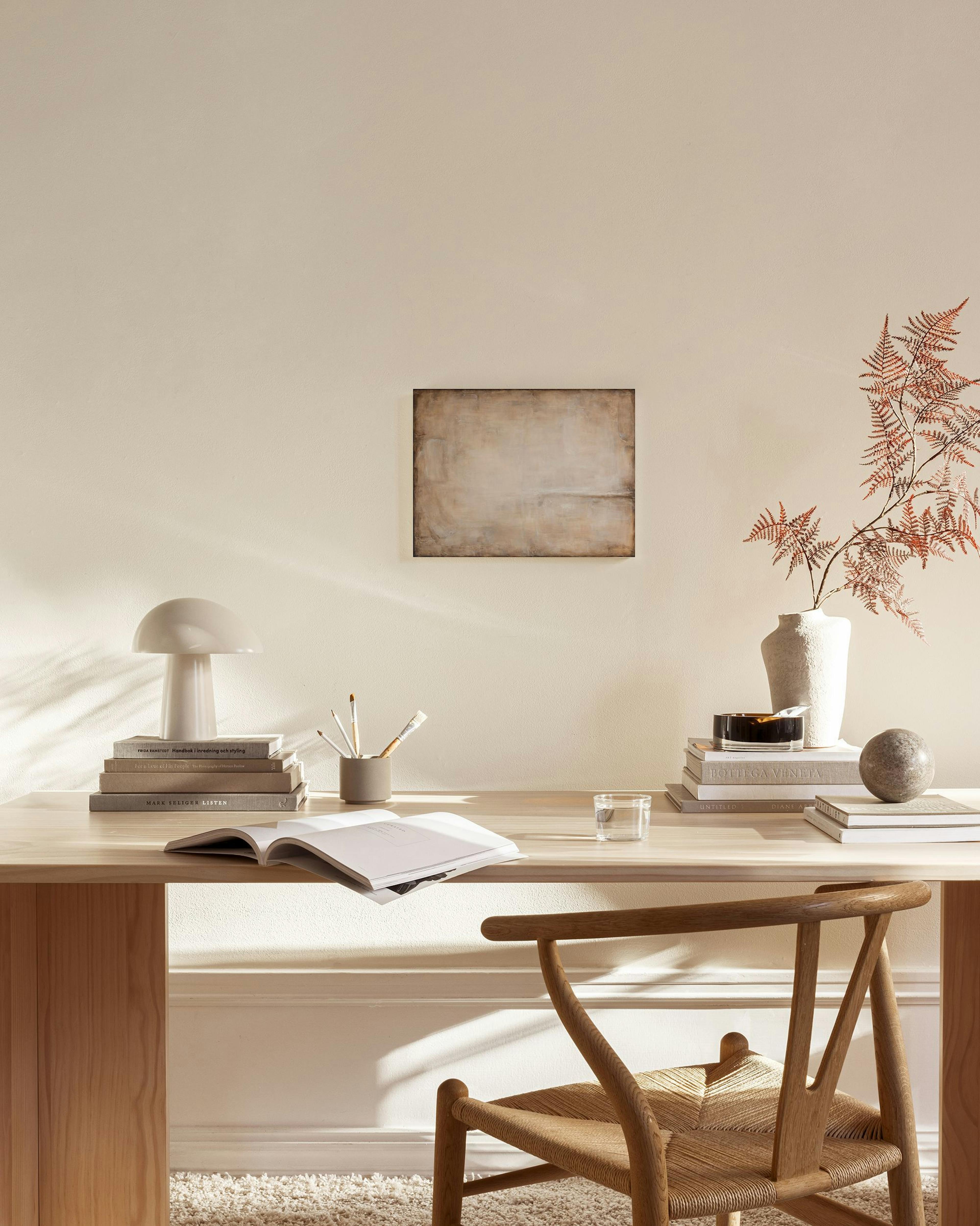 Abstrakti kanvaasi beigen ja ruskean sävyissä modernissa olohuoneessa puisen tason yläpuolella.