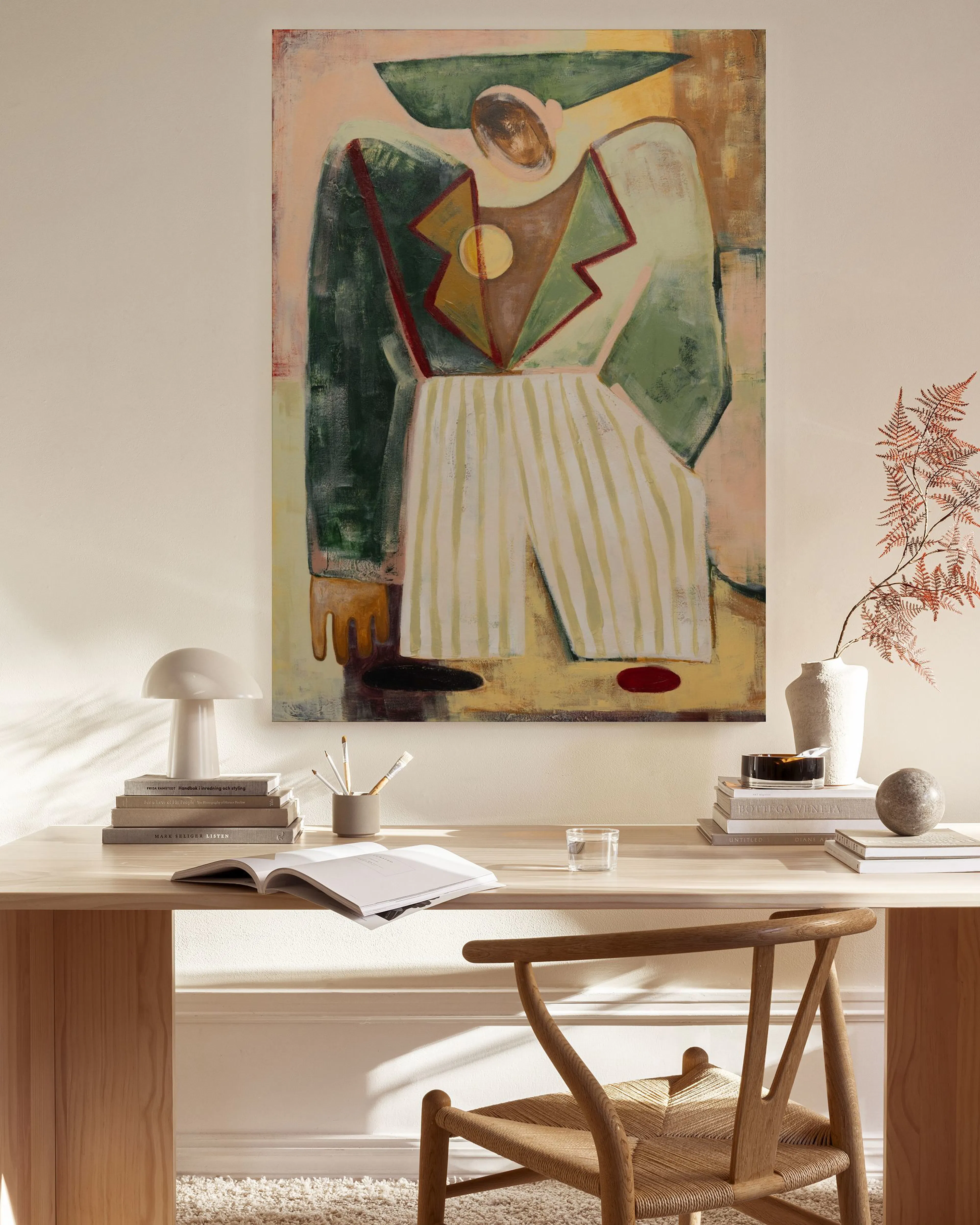 Abstract figure in green, red, and beige with striped pants, hanging above a wooden console in a modern living room.