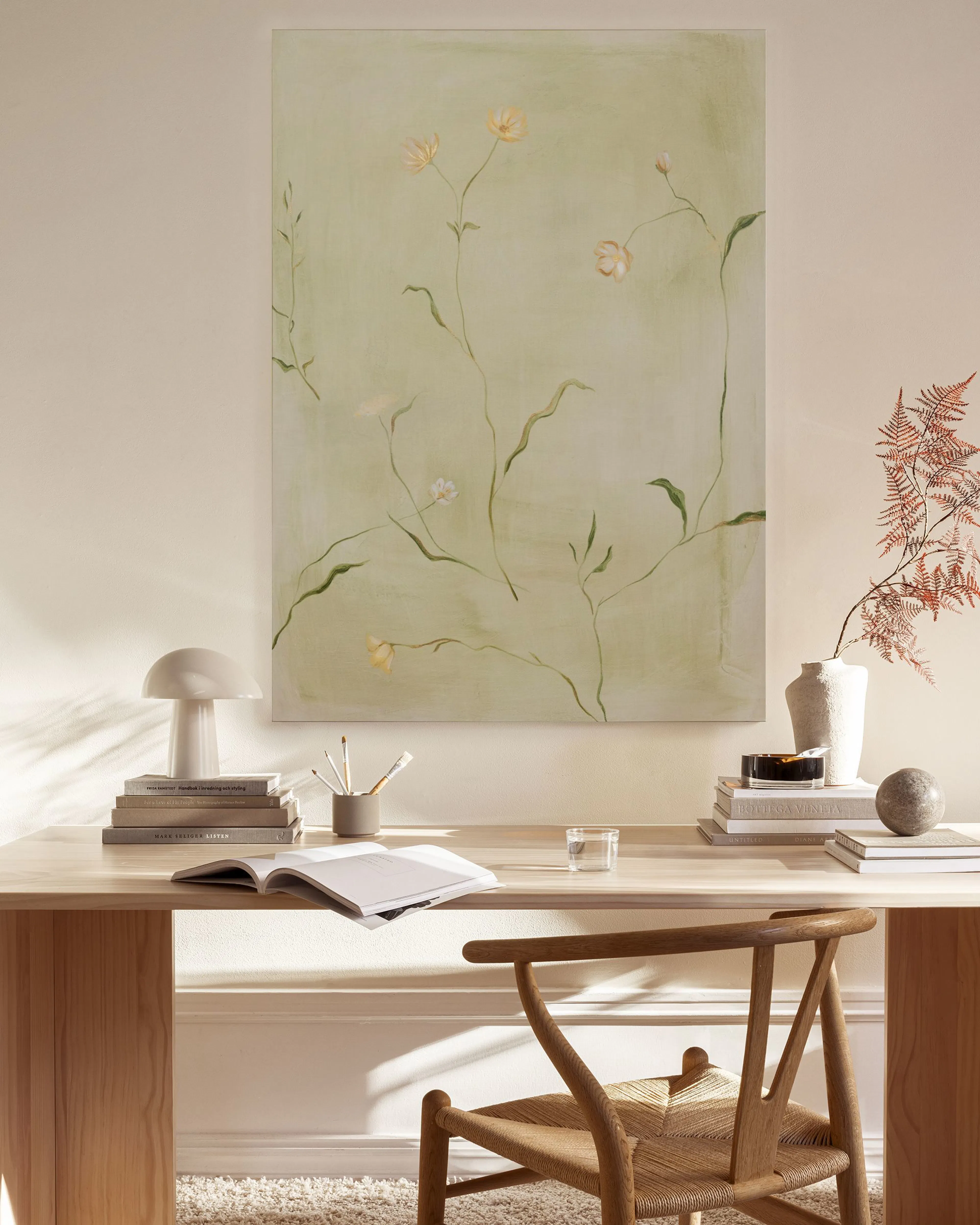 A canvas print of delicate light yellow flowers and green stems on a pale green background, hanging in a neutral-toned living ro