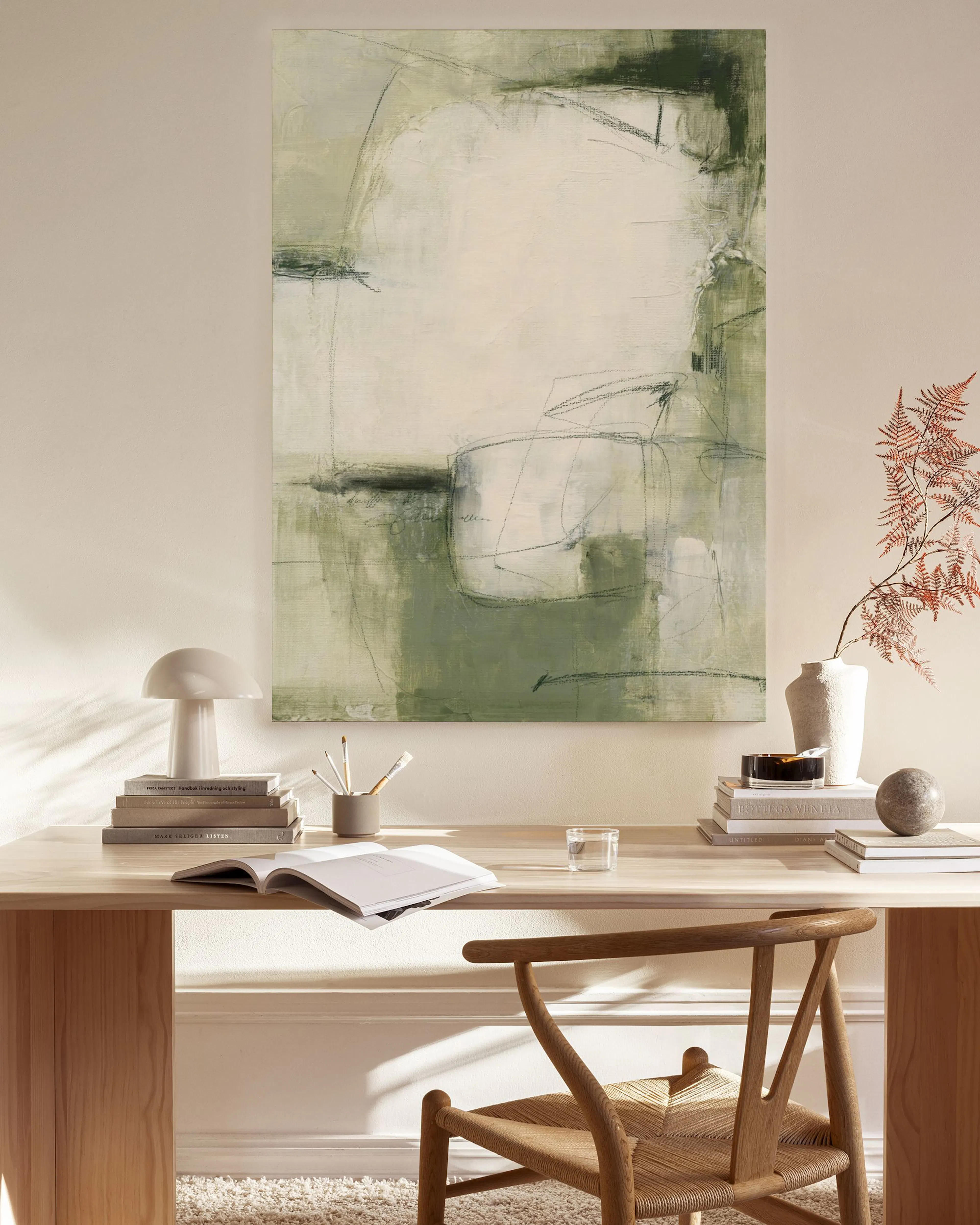 Un lienzo con formas abstractas en tonos verdes y blanco, colgado sobre un mueble en una sala de estar moderna.