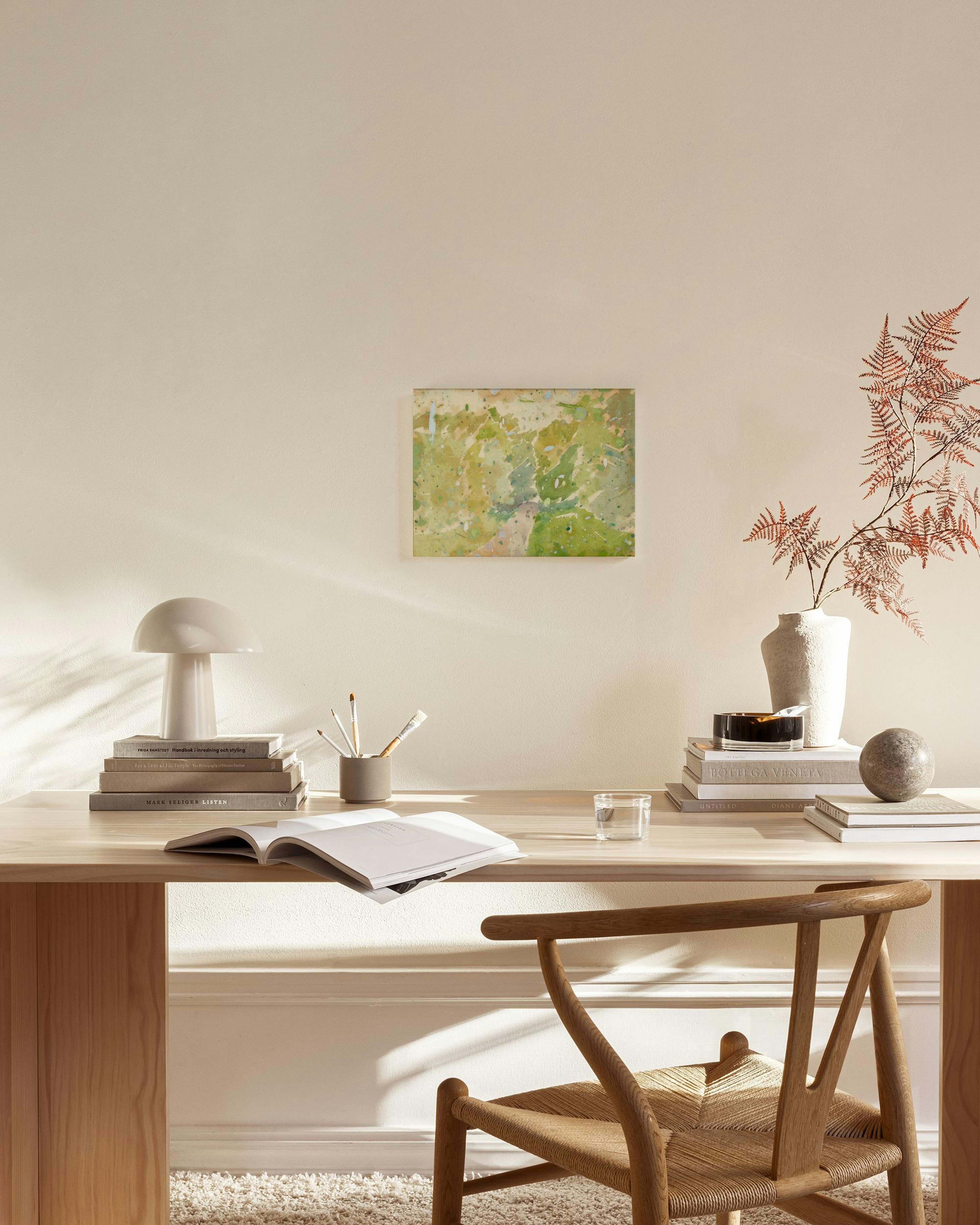 Canvas met groene en beige vlekken in een lichte woonkamer met houten meubels en een glazen salontafel.