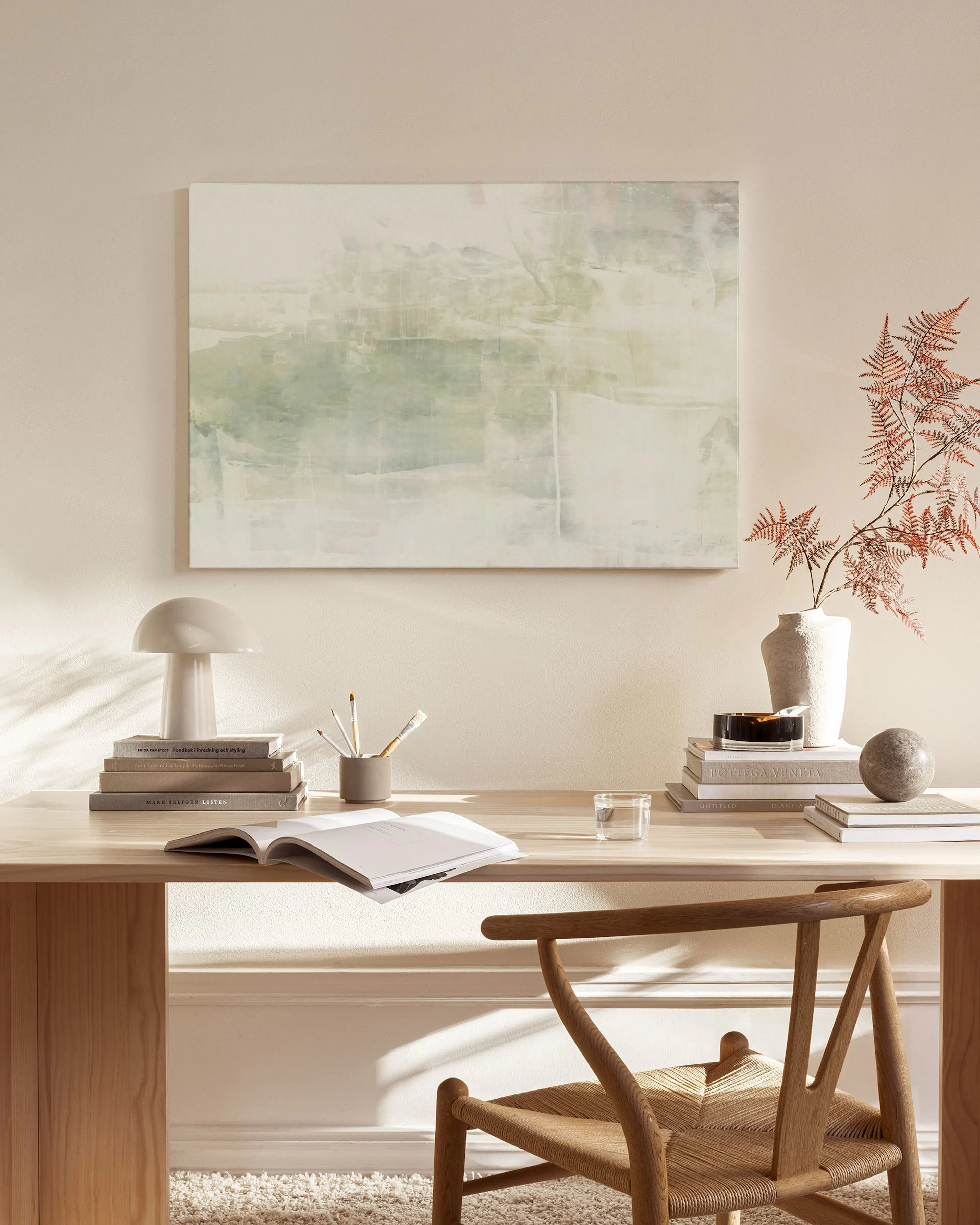 An abstract canvas print with soft green and muted white hues, hanging above a timber console in a modern living space.