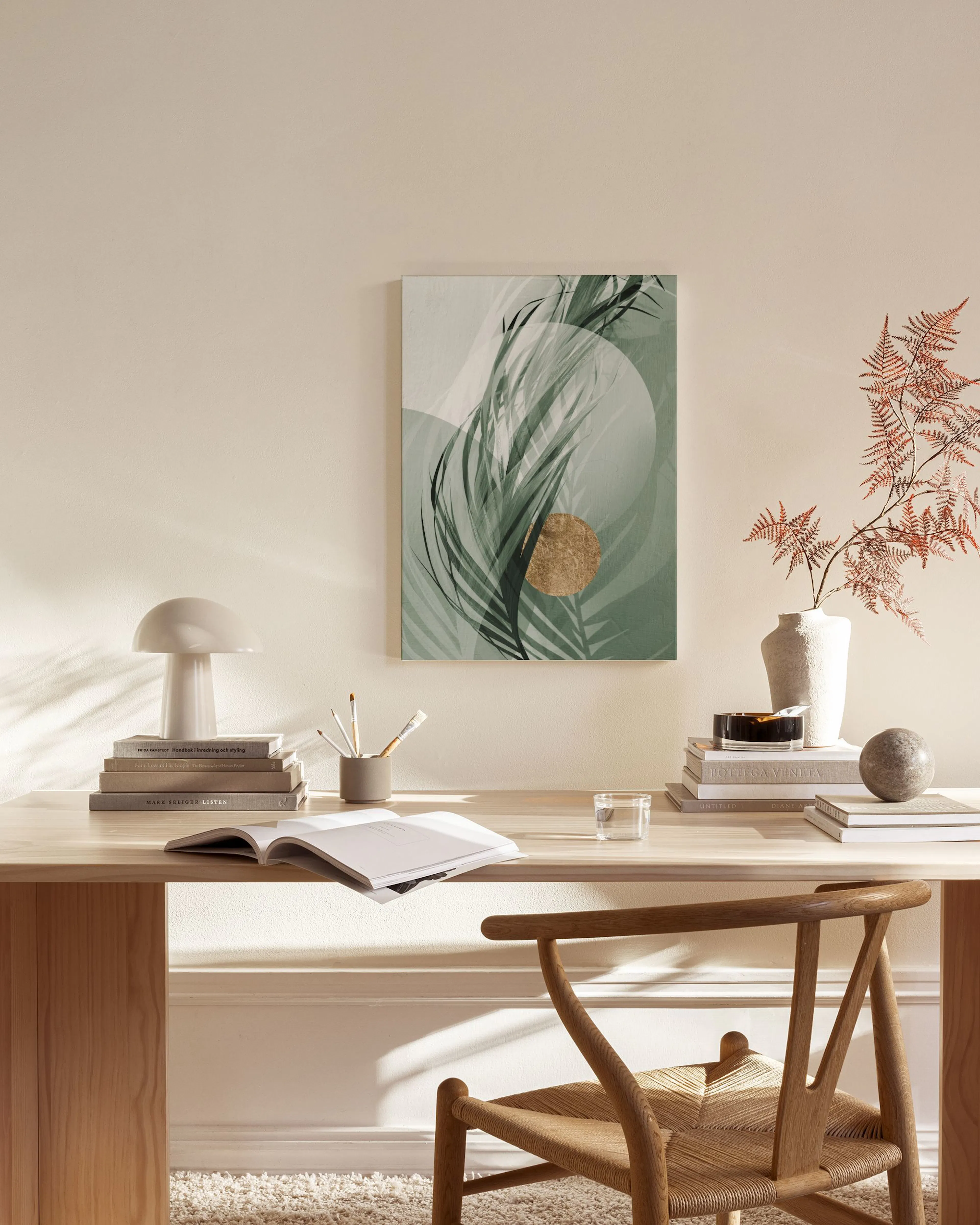 Tropical leaf print with a gold circle and abstract shapes, hanging in a modern living room.