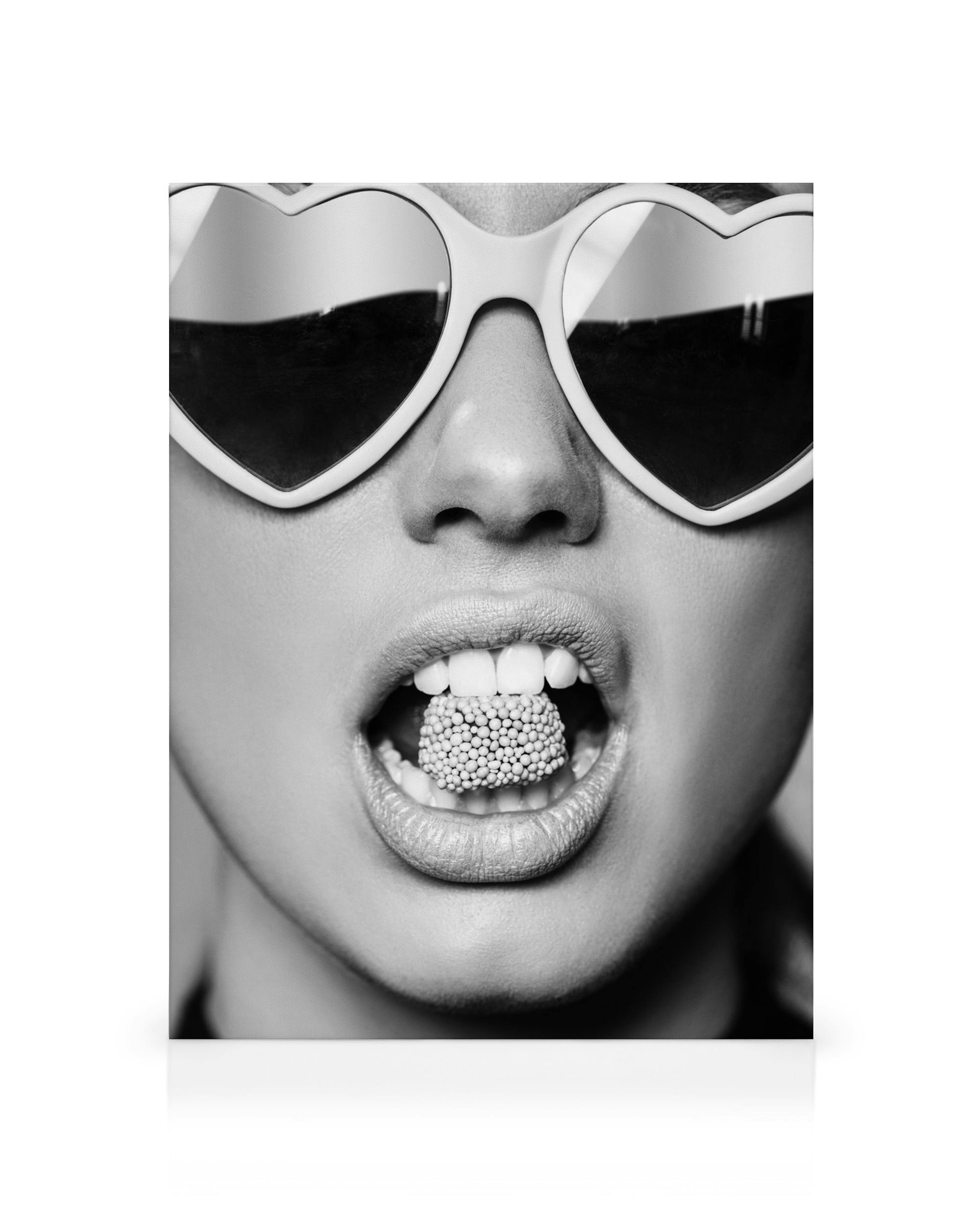 Čiernobiely obraz na plátne: žena s okuliarmi v tvare srdca a cukríkom v ústach. Pop art štýl, moderné umenie.