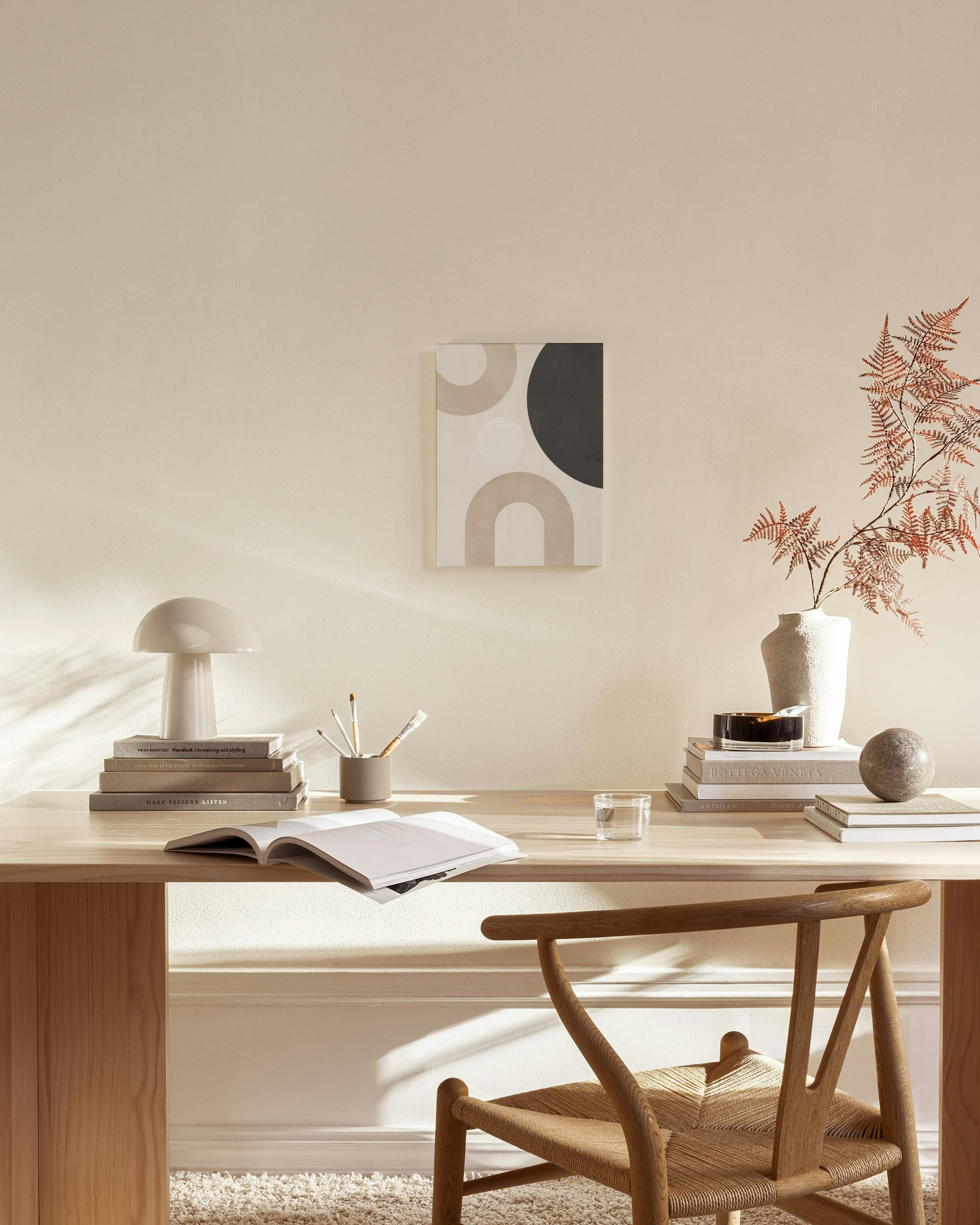 Abstract print with beige, black, and white circles and arches, hanging in a minimalist living room above a wooden console.