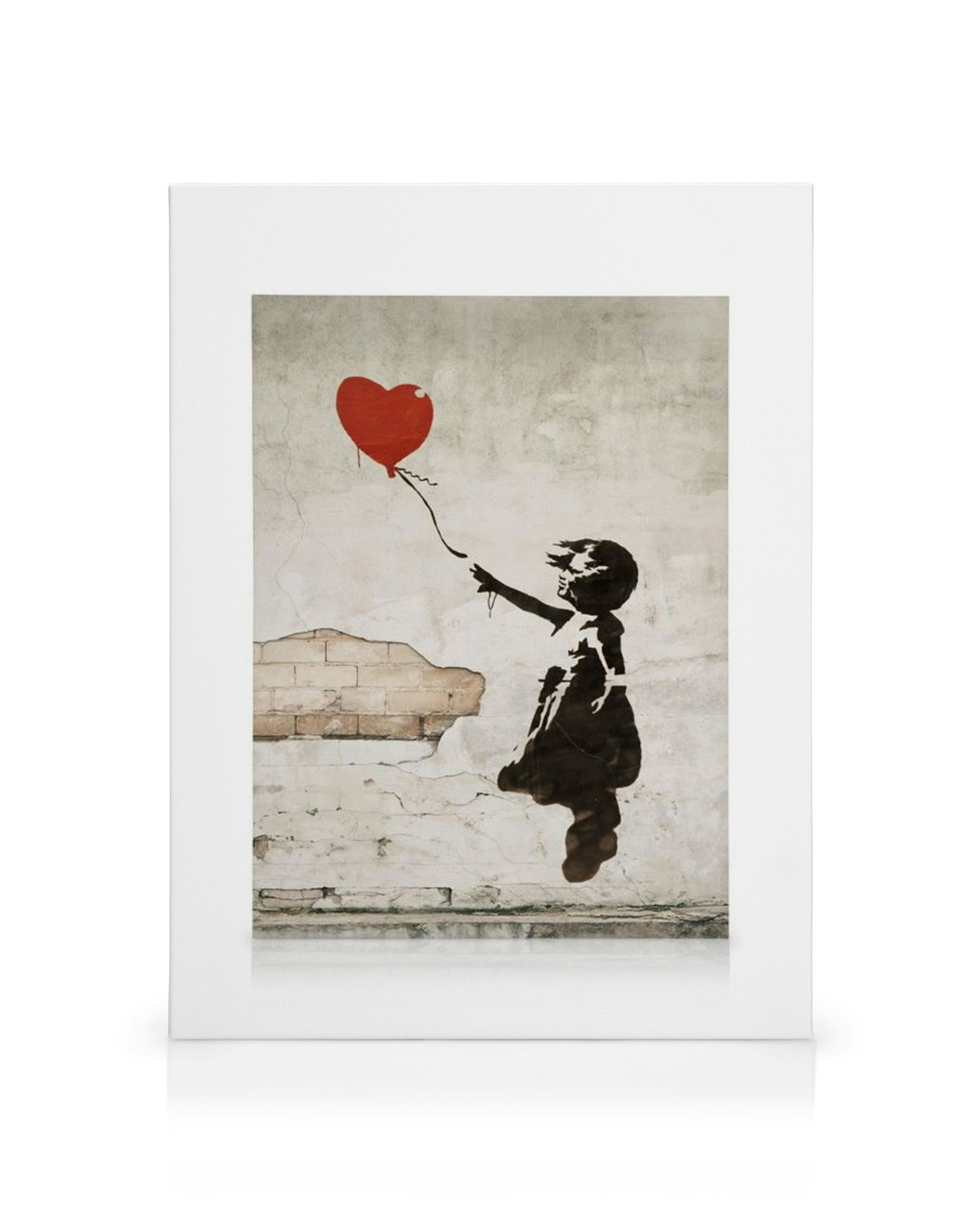 Svartvit canvastavla av ett barn som sträcker sig efter en röd, hjärtformad ballong mot en rustik tegelvägg.
