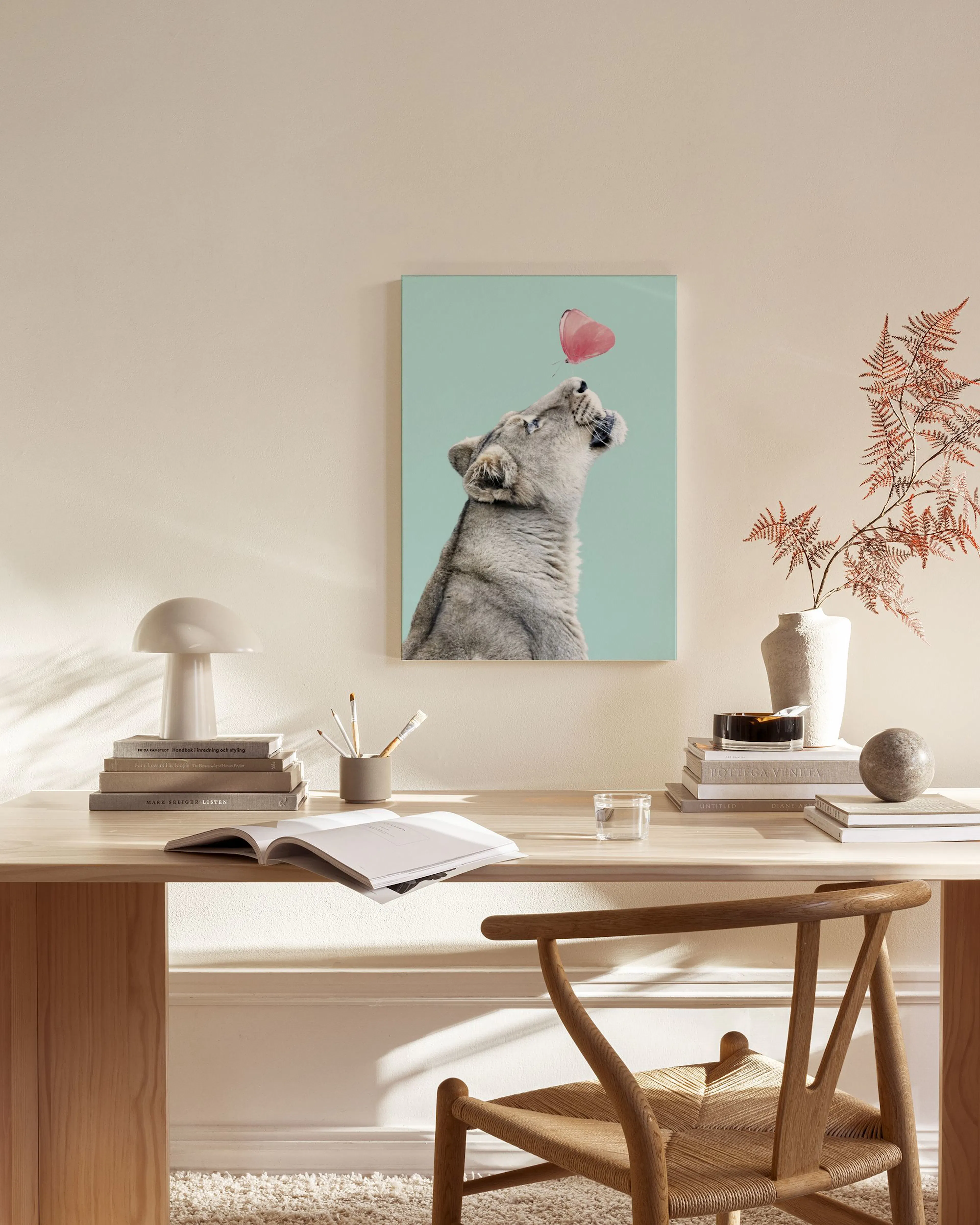 Una stampa su tela con un leone che guarda una farfalla rosa, appesa in un soggiorno moderno.